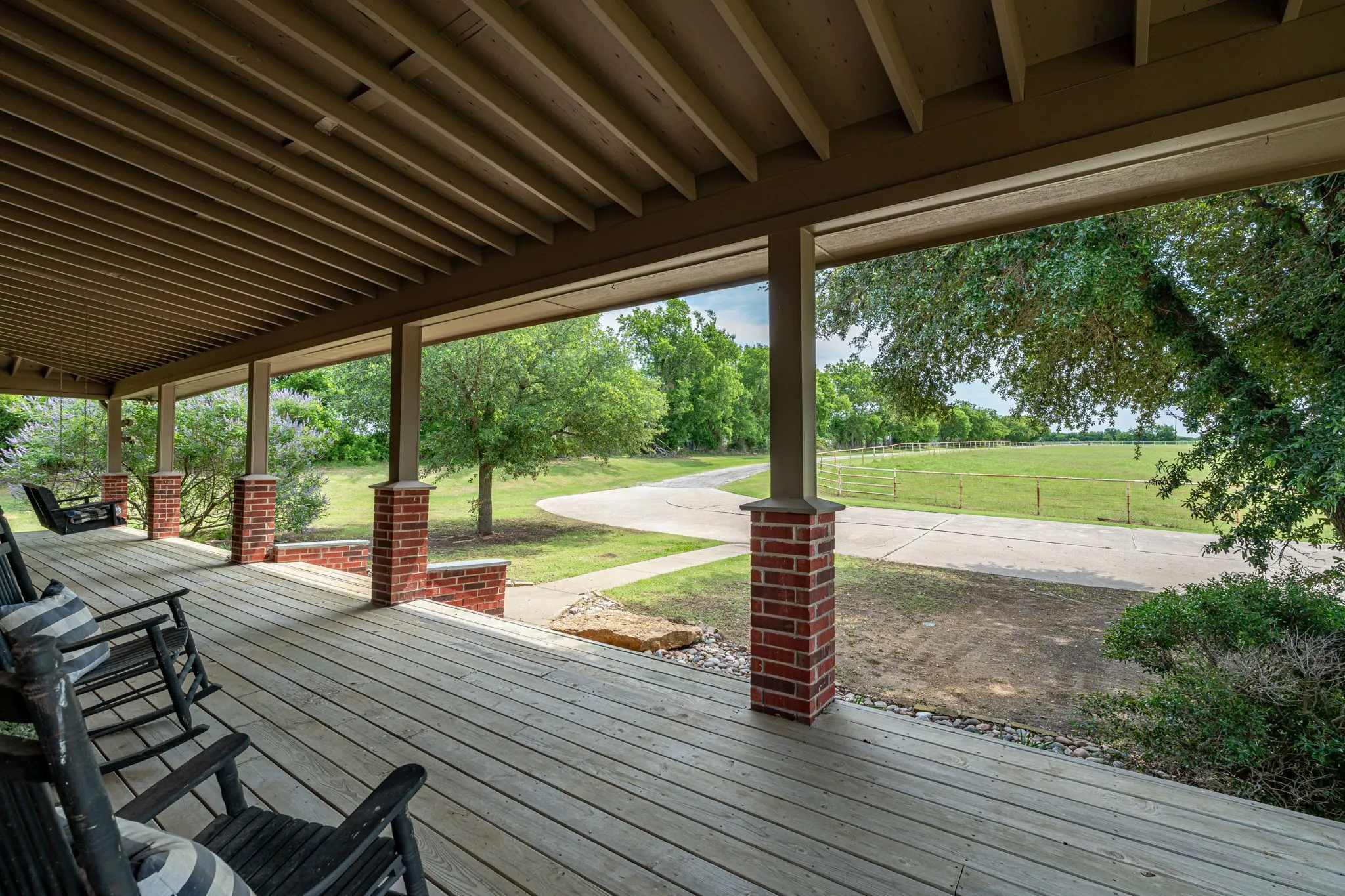 Expansive covered porch featuring wood-finish decking, brick pillars, and a ceiling with exposed beams
