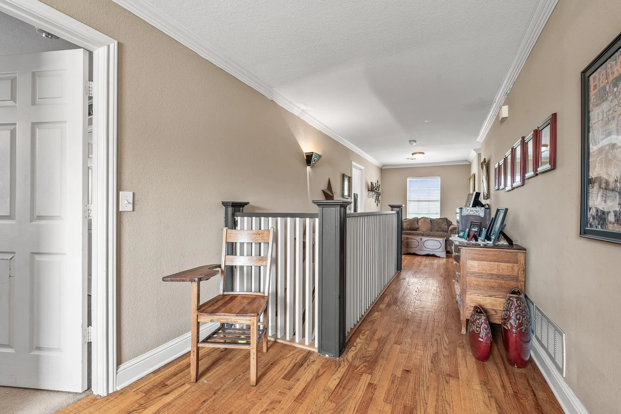 Hardwood flooring extends throughout this upper-level hallway, complemented by neutral wall paint and white crown molding