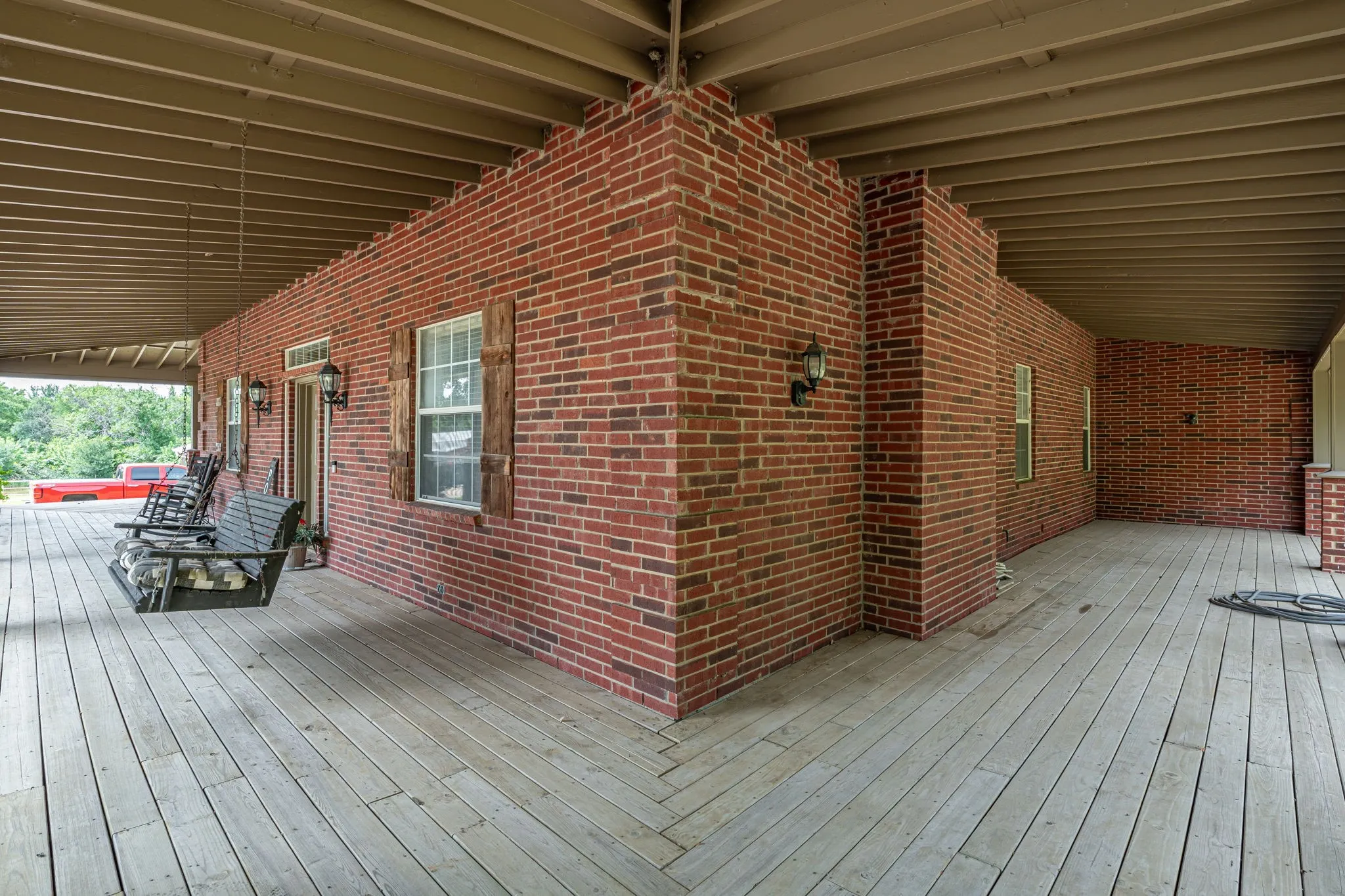 Expansive covered porch featuring a red brick facade, wood-plank flooring, and exposed ceiling joists