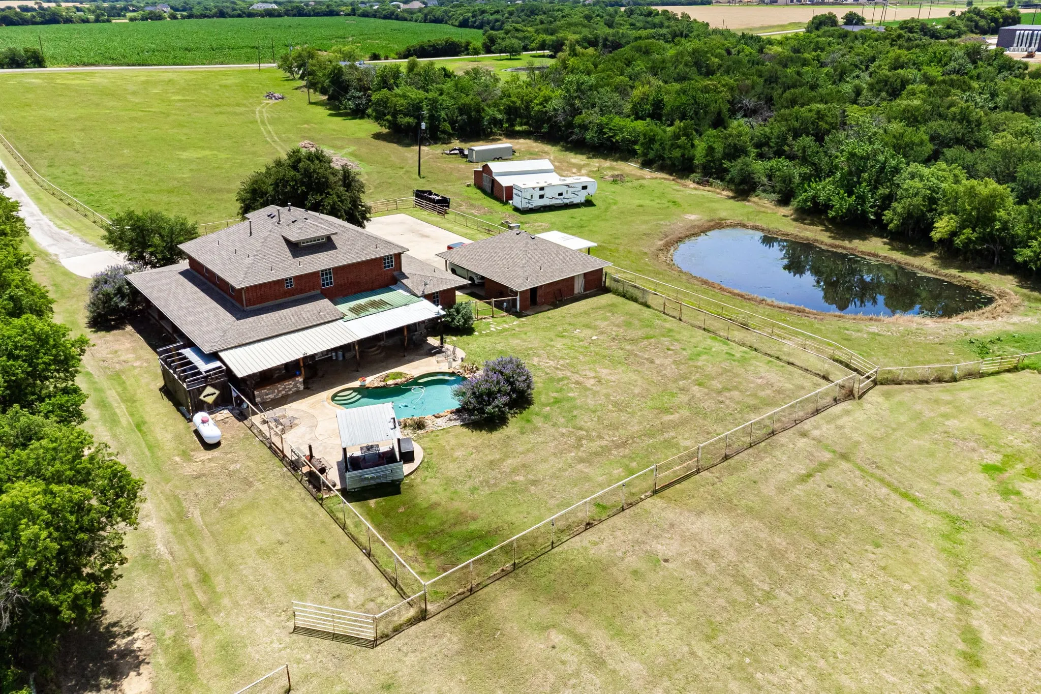 Expansive property featuring a brick residence, a detached auxiliary building, a dedicated pool area, and a private pond