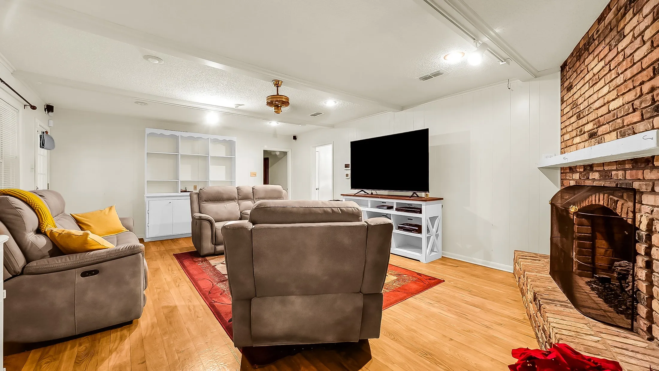 Living area featuring a brick fireplace with a white mantel, wood-finish flooring, and white wall paneling