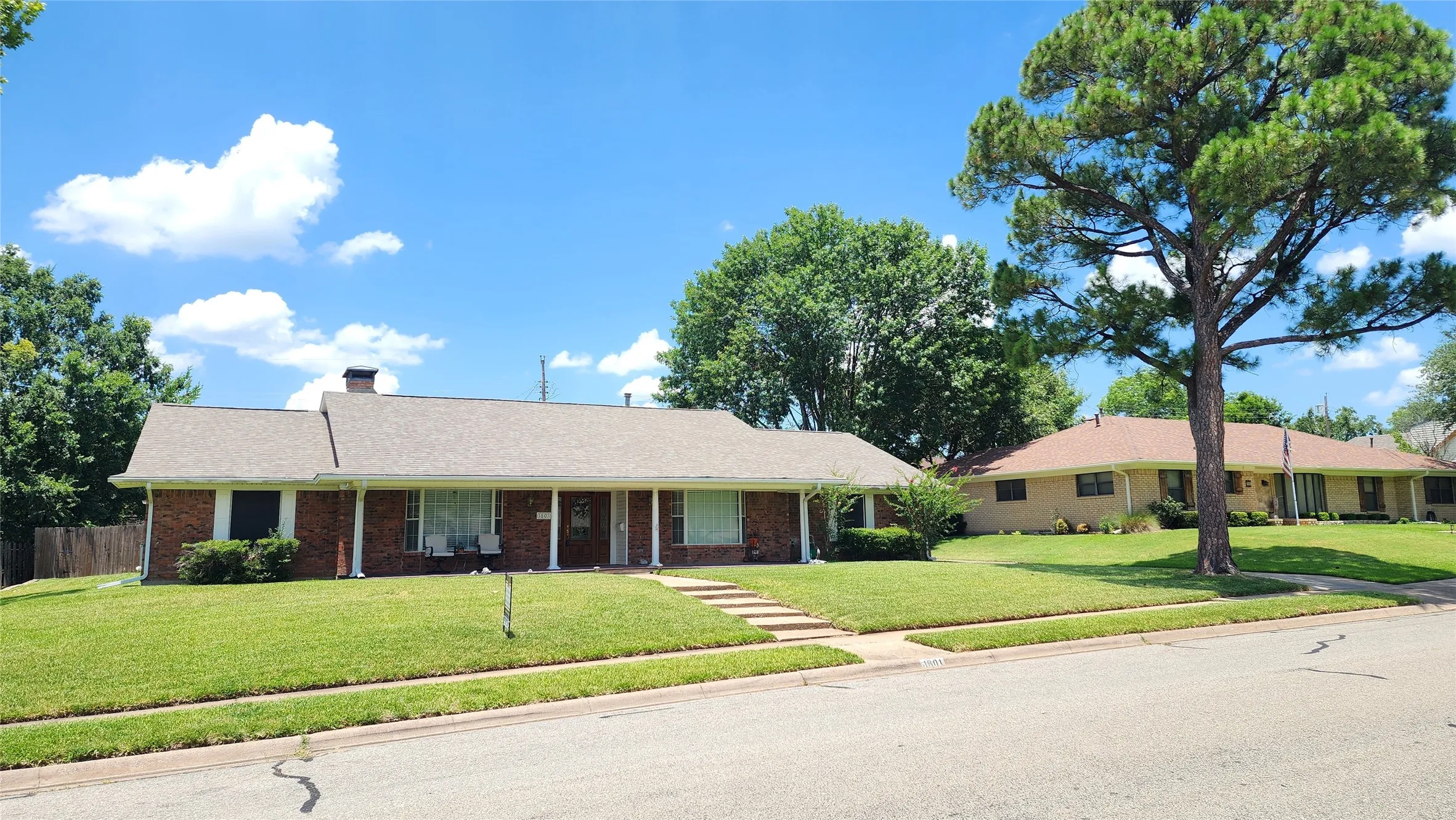 Traditional brick residence featuring a prominent front lawn and mature trees