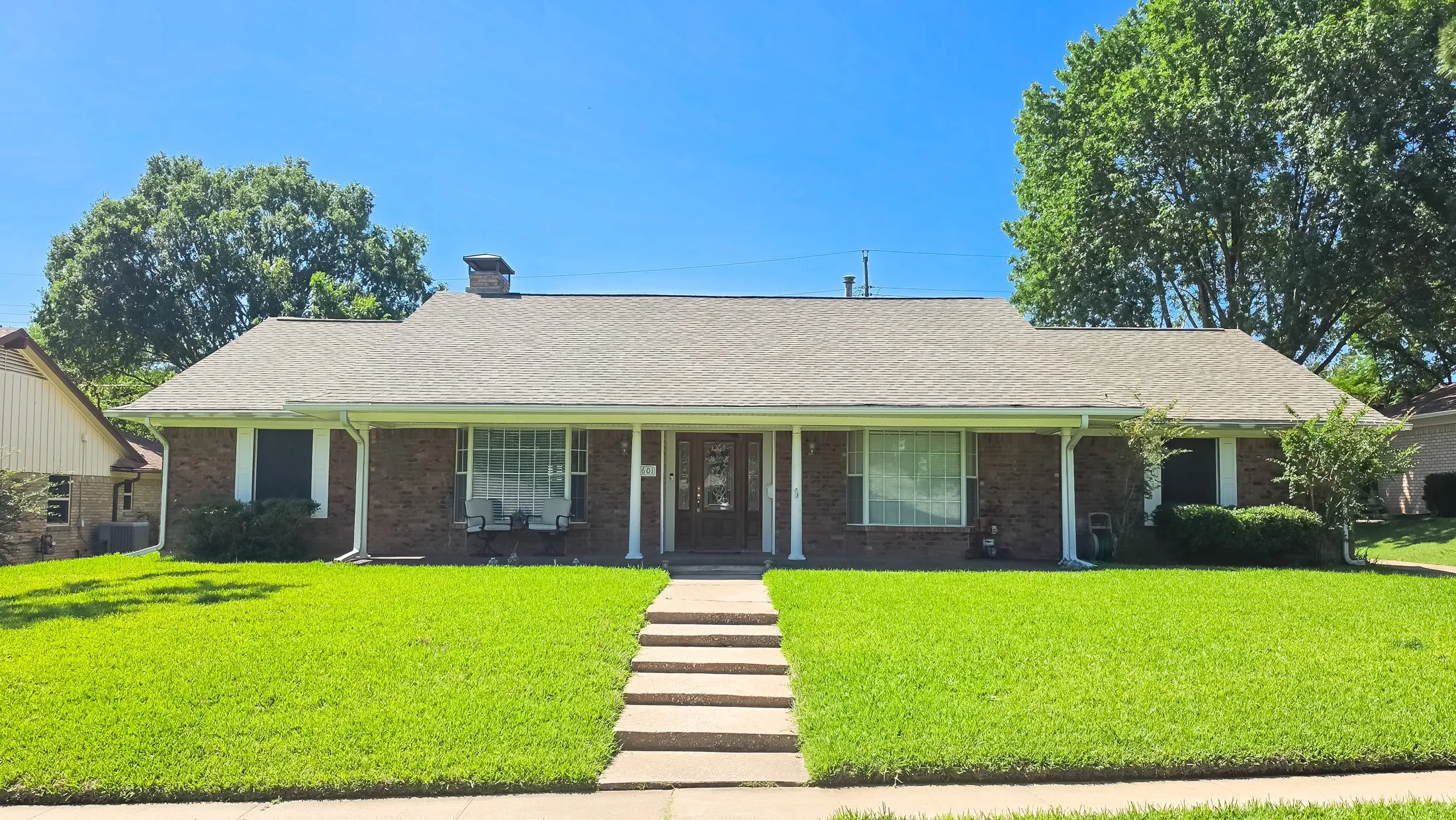 Brick exterior with a gabled roofline, front porch columns, a concrete walkway, and a manicured front lawn