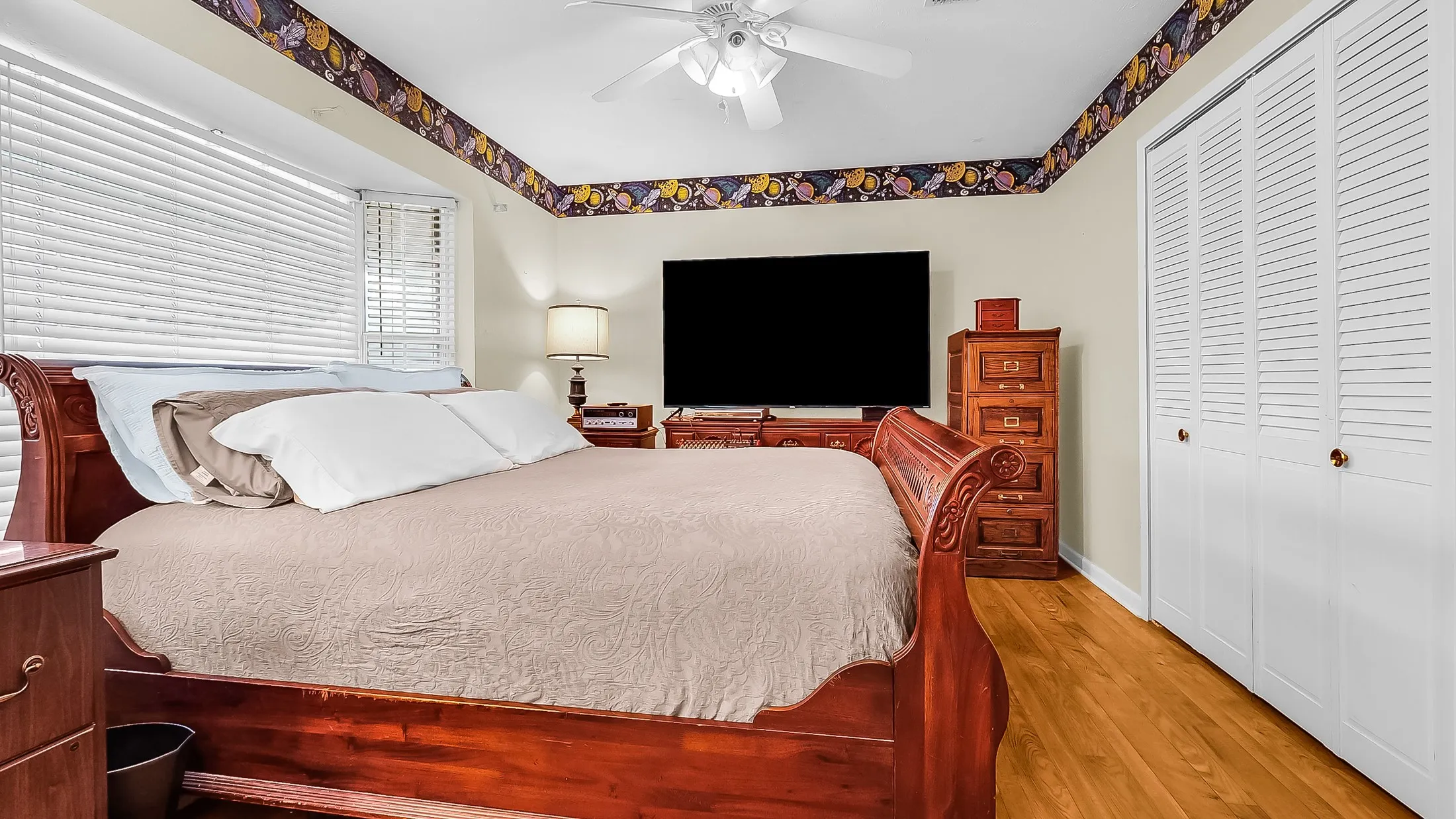 Bedroom featuring wood-finish flooring, white louvered bi-fold closet doors, a white ceiling fan, and window blinds