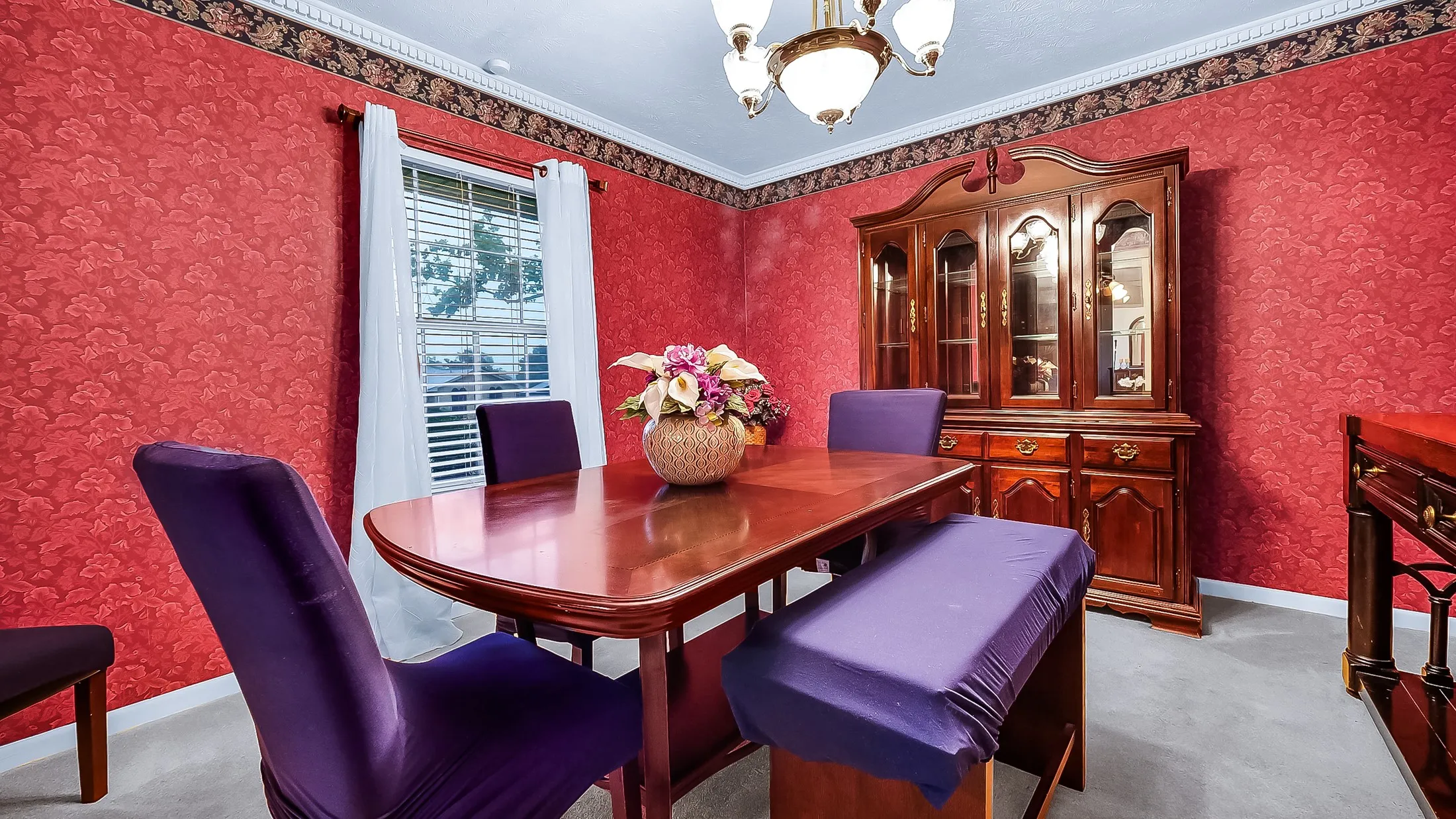 Dining area featuring red patterned wall covering, a decorative border, and a window with blinds