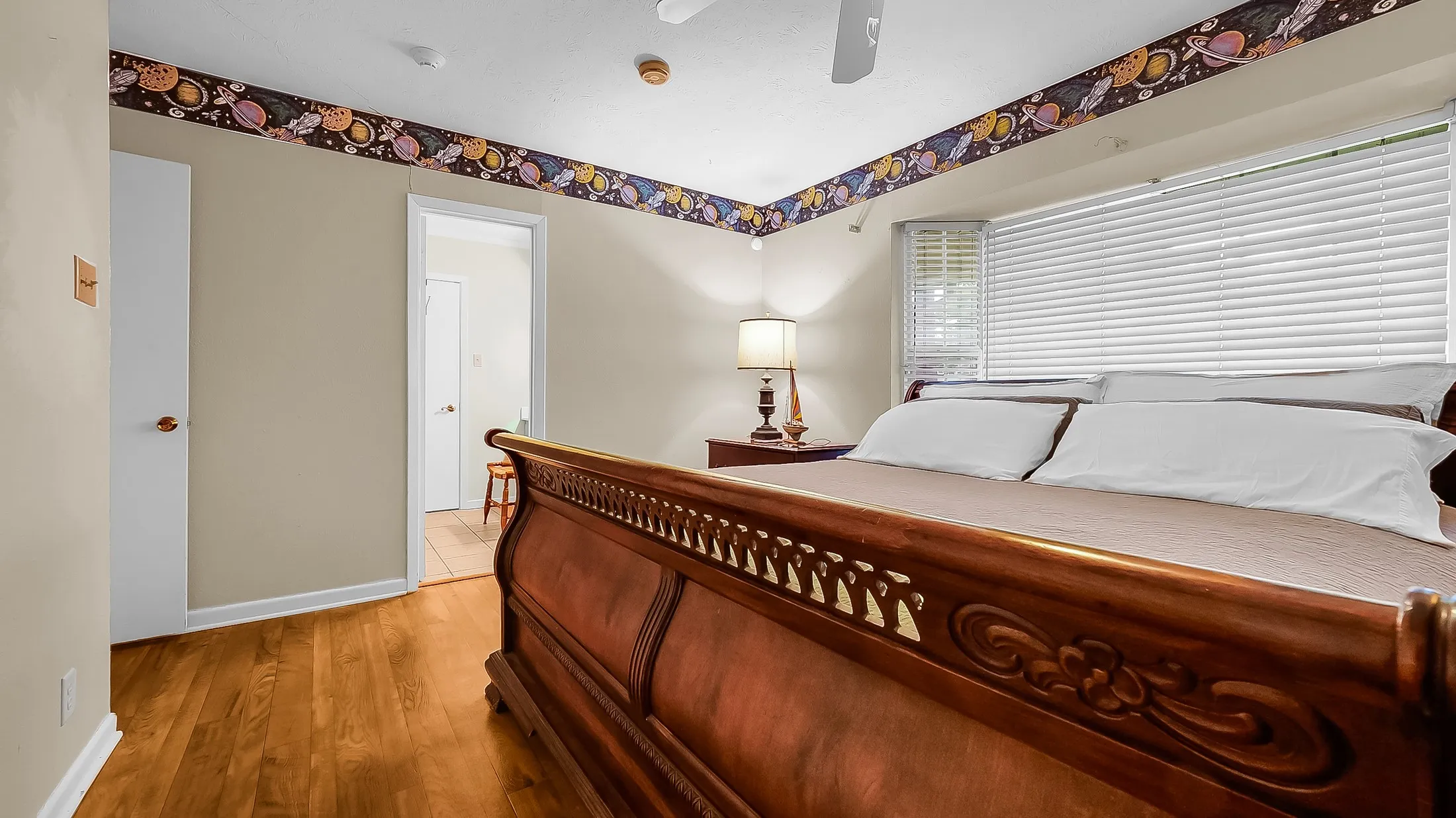 Spacious room featuring wood-finish flooring, a ceiling fan, and a large window with horizontal blinds and shutters