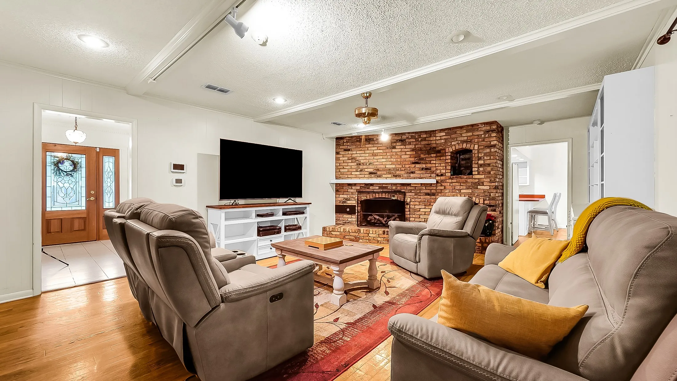 Spacious living area featuring a brick fireplace, wood-finish flooring, and recessed lighting