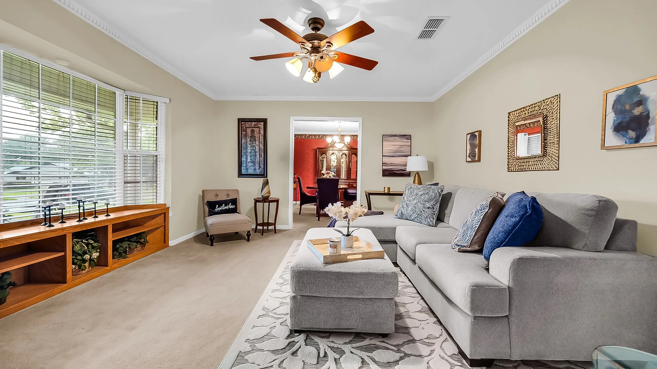 Spacious living area featuring a ceiling fan with integrated lighting, crown molding, and neutral wall tones