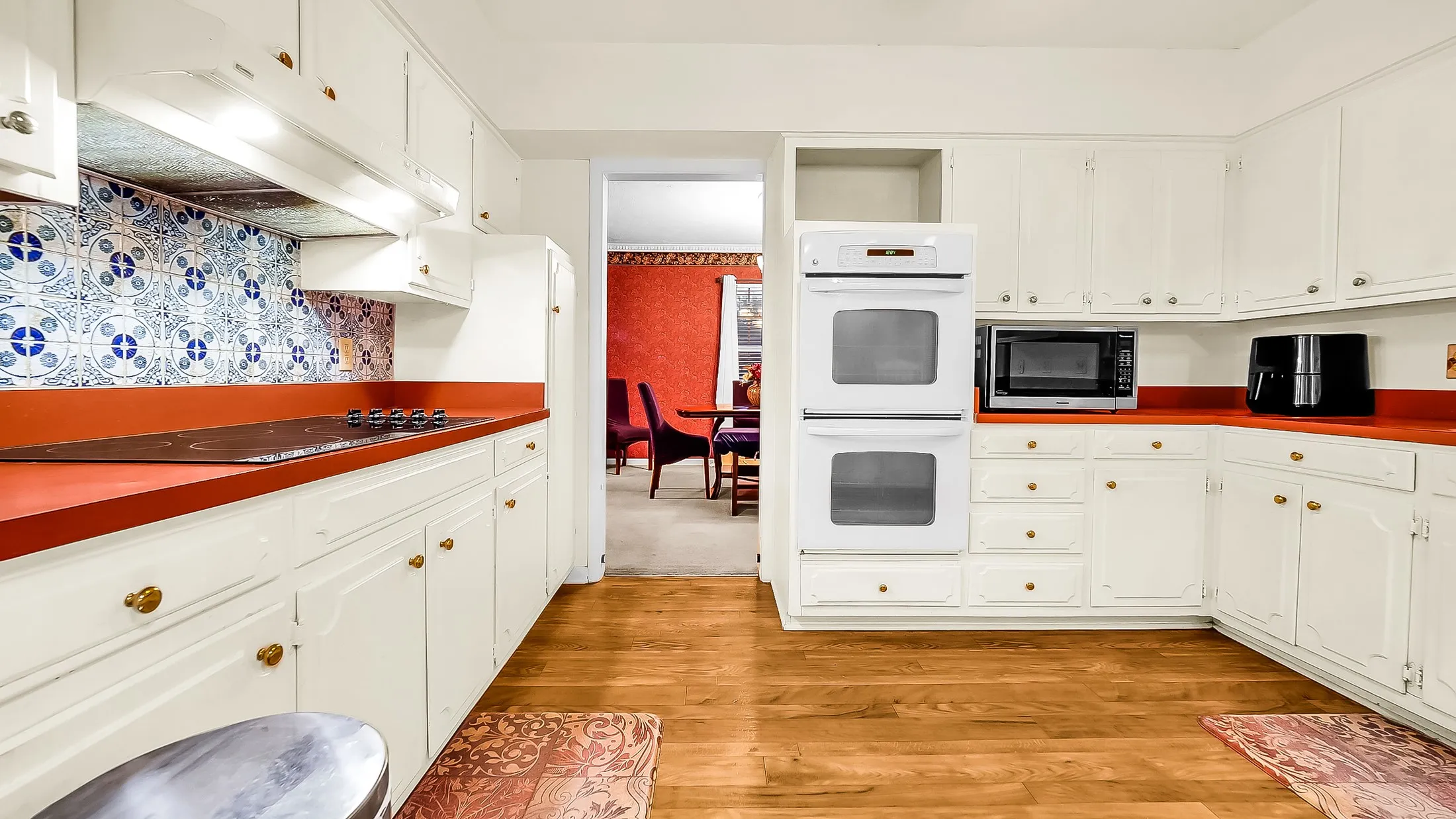 Kitchen featuring wood-finish flooring, white cabinetry with brass-toned hardware, red countertops, a patterned tile backsplash, and a built-in double oven