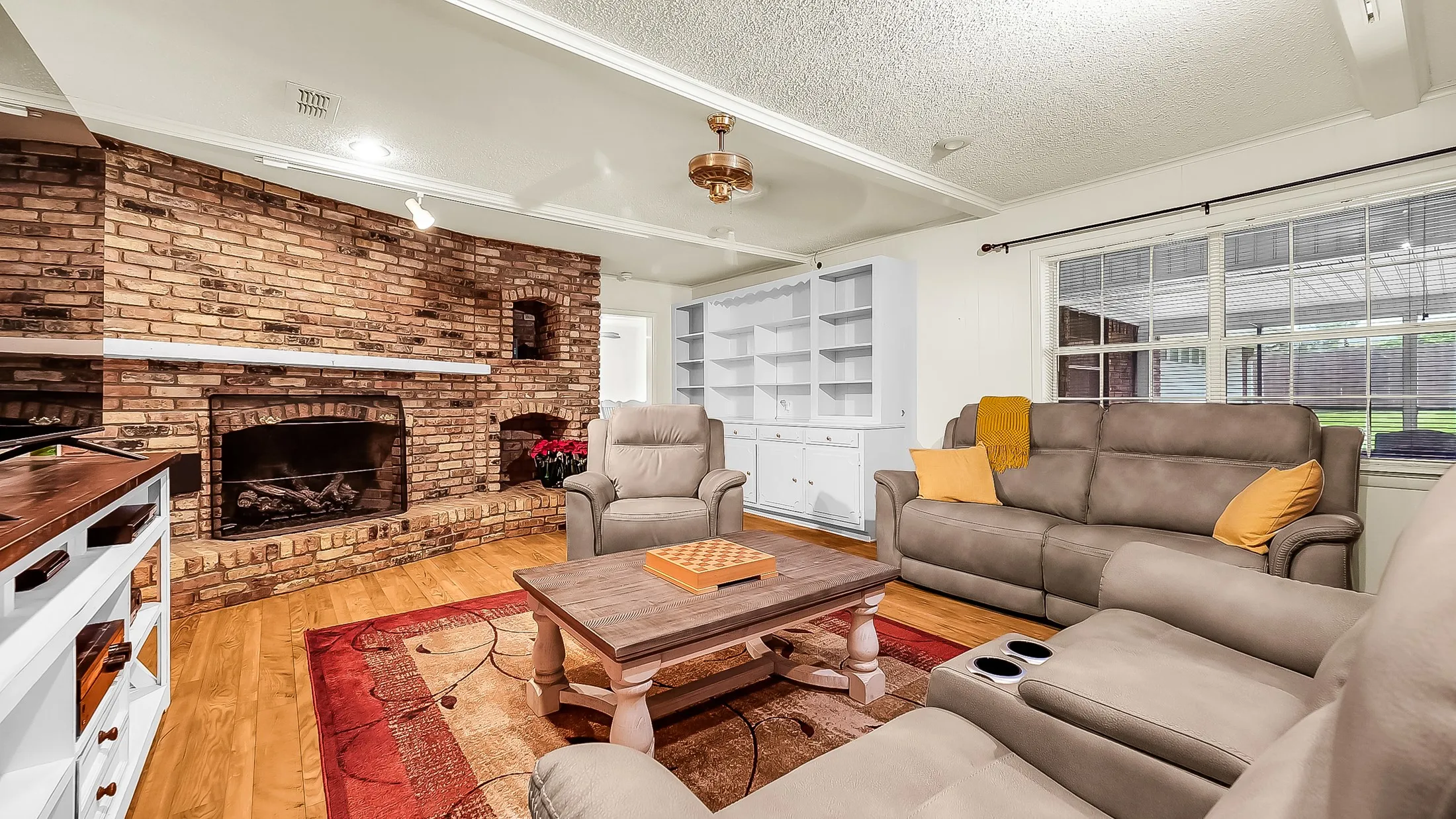 Exposed brick fireplace with a stone hearth, wood-finish flooring, built-in shelving, white trim, and multiple large windows