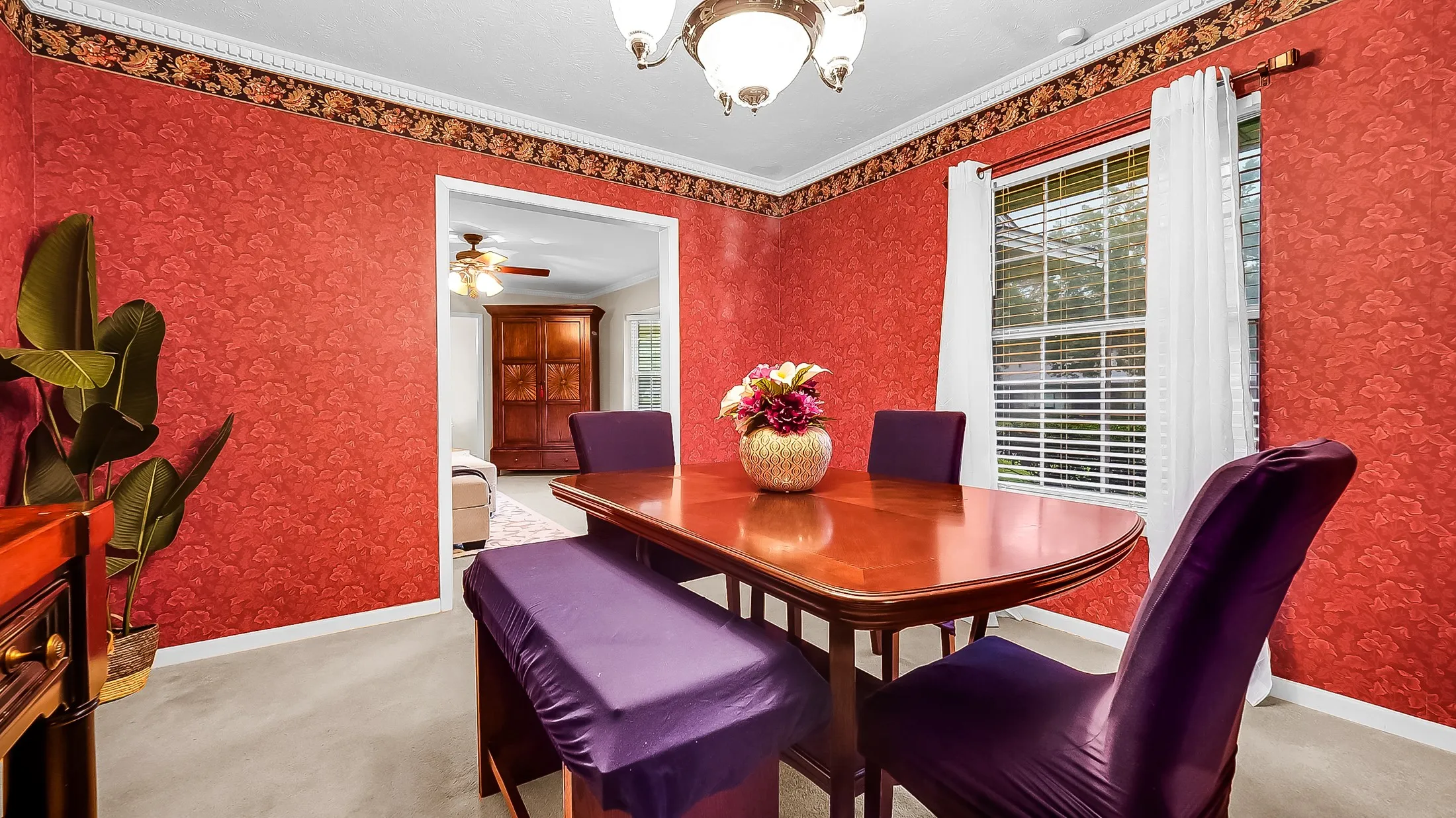 Formal dining area featuring patterned red walls, white crown molding, and a decorative border