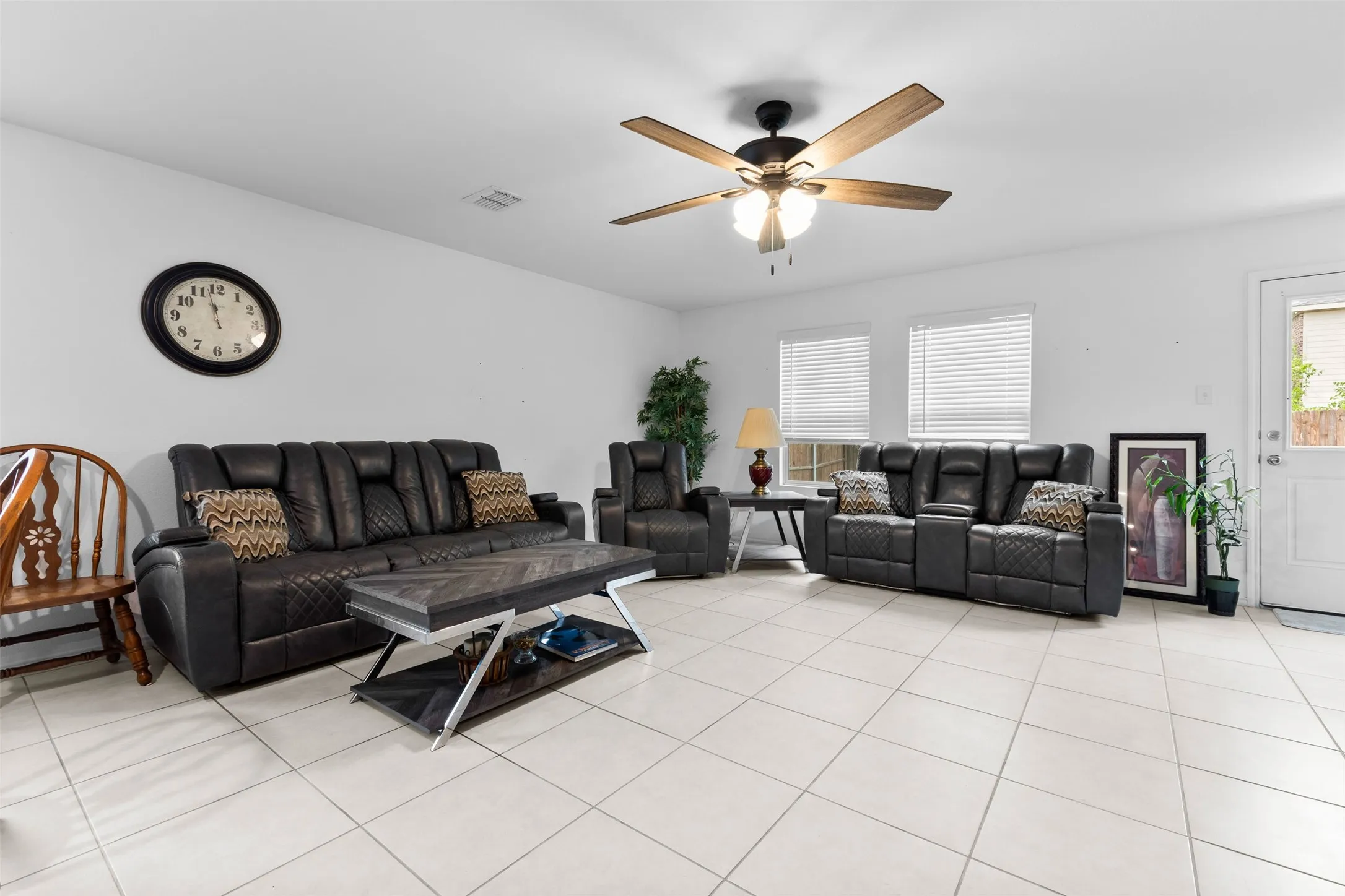 Bright living area featuring light-toned tile flooring, white walls, and a ceiling fan with integrated lighting