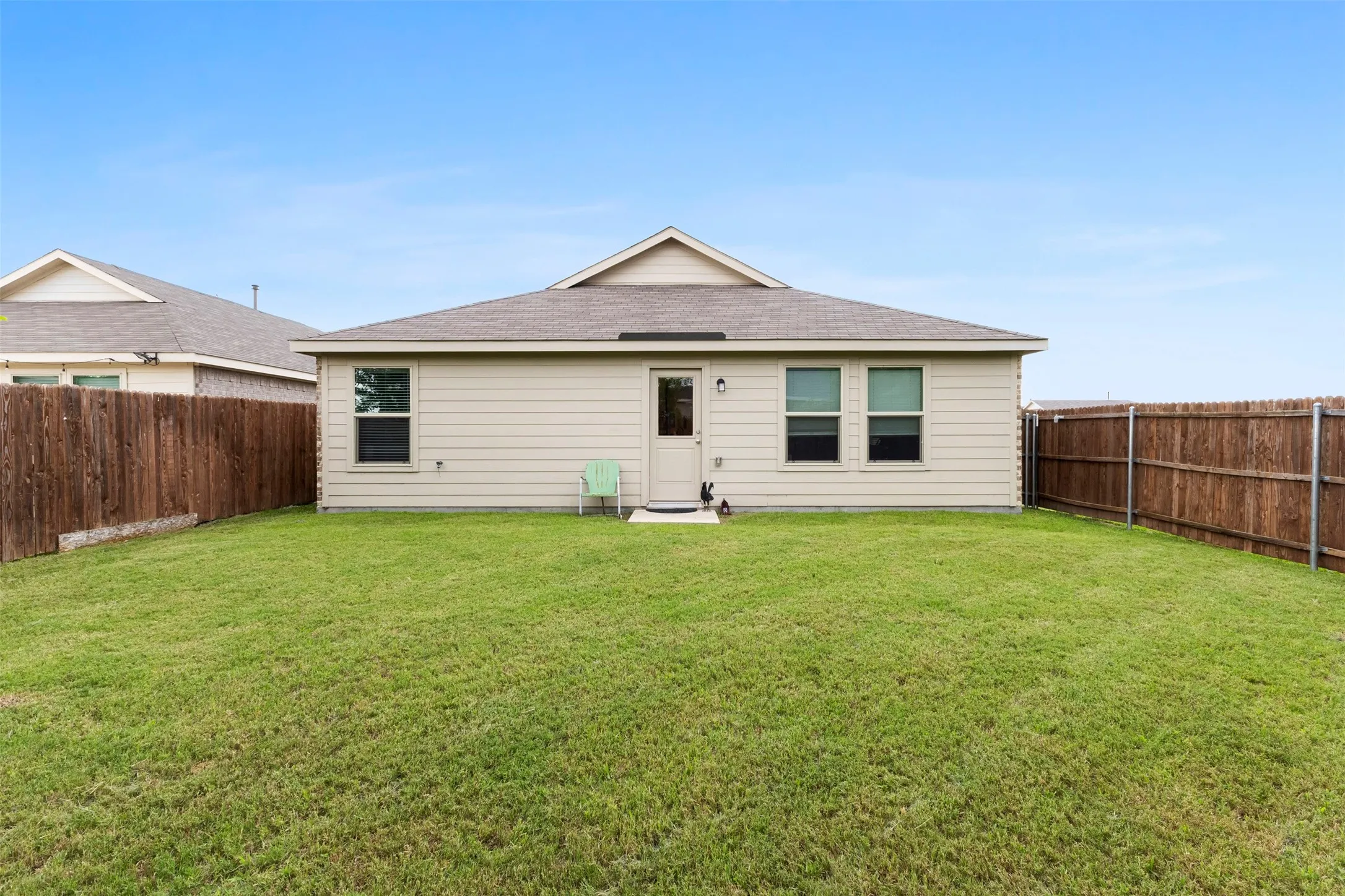 Expansive backyard featuring a large grass lawn, full perimeter wood fencing, and a rear exterior with multiple windows