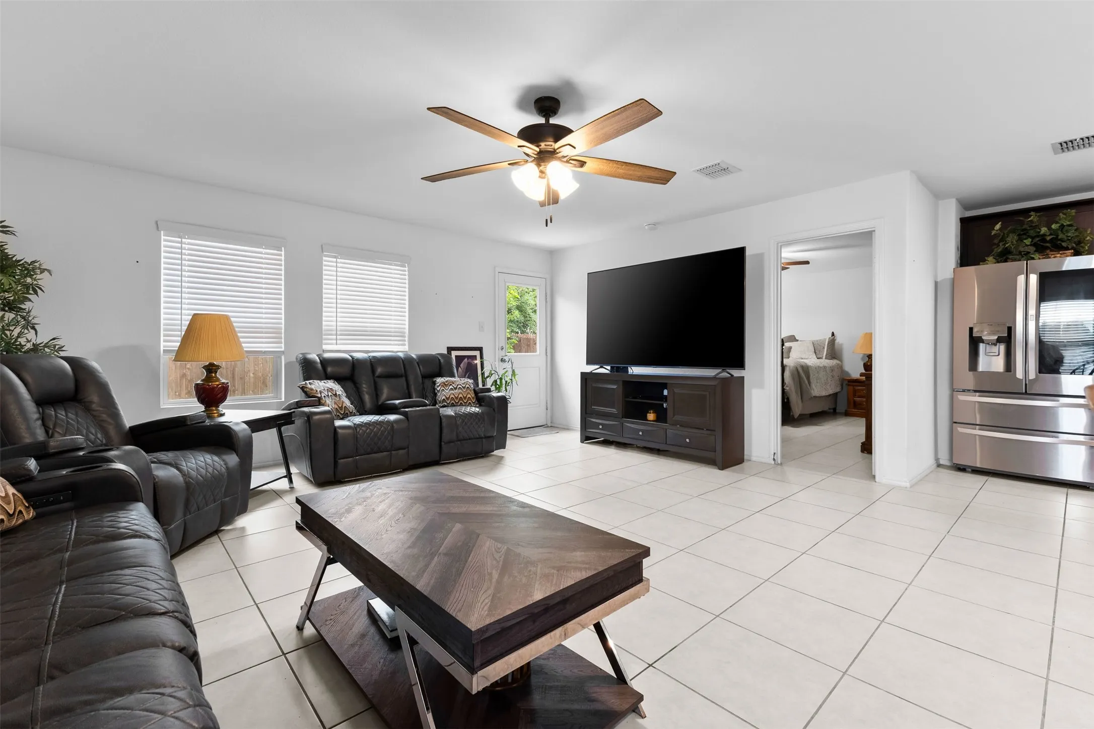 Spacious living area featuring light-toned tile flooring, a ceiling fan with integrated lighting, and white walls