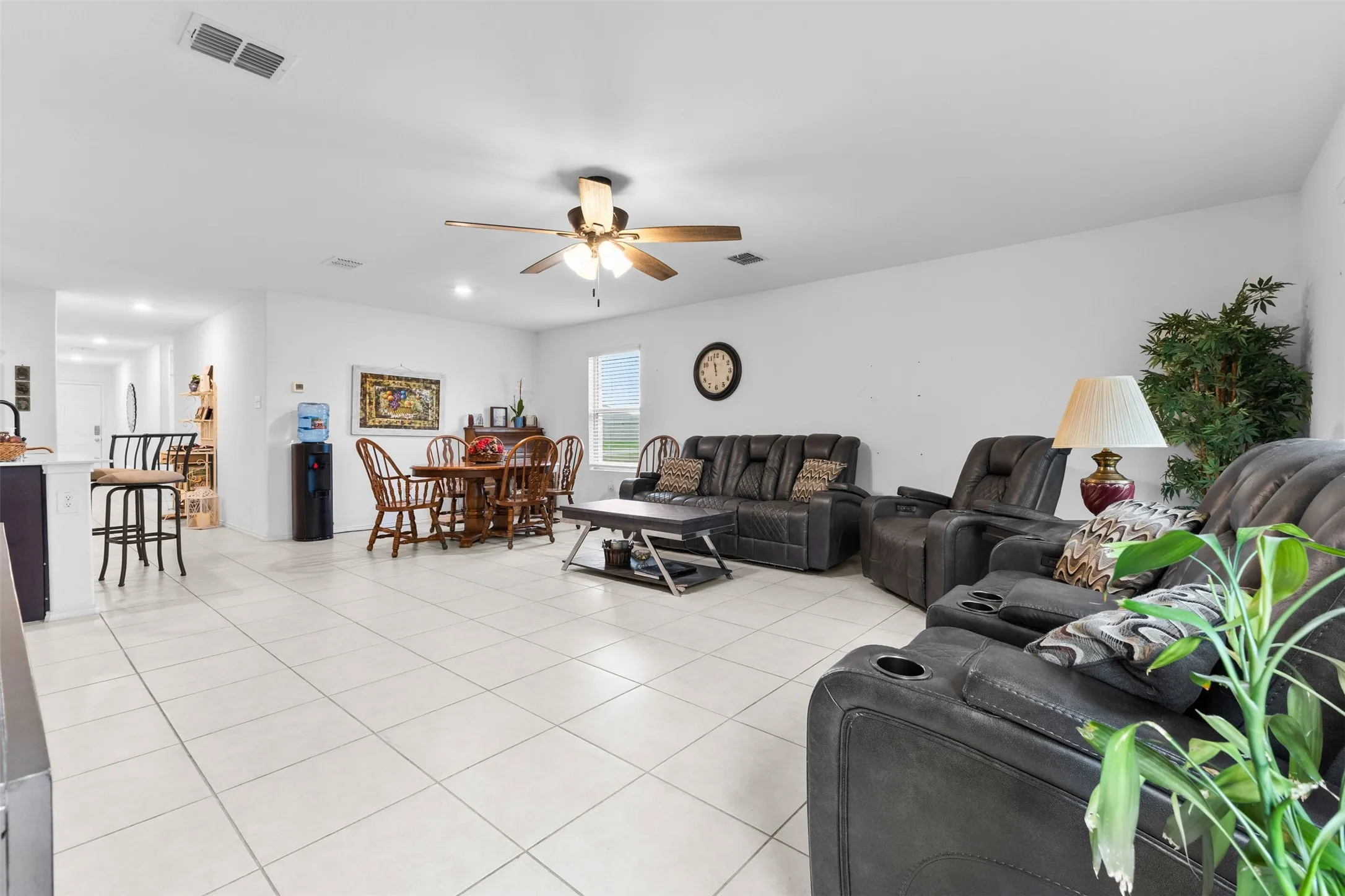 Open-concept living space featuring light-colored tile flooring, white walls, and a ceiling fan