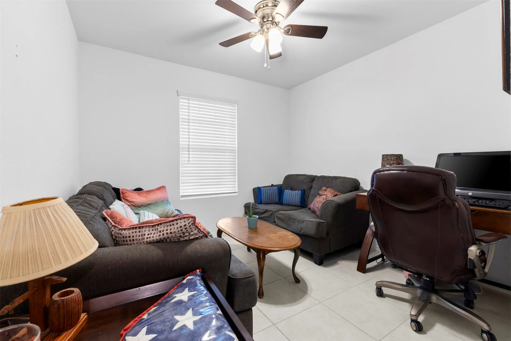 Room featuring white walls, tile flooring, a window with horizontal blinds, and a ceiling fan with integrated lighting
