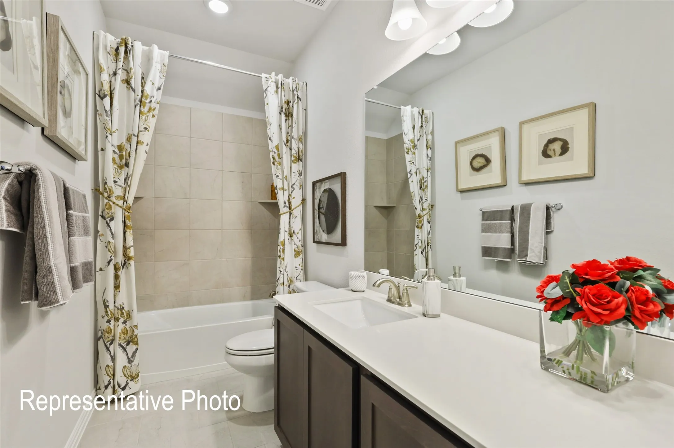 Bathroom featuring a white bathtub, beige tiled shower surround, dark wood-finish vanity with a light-toned countertop, and a large mirror