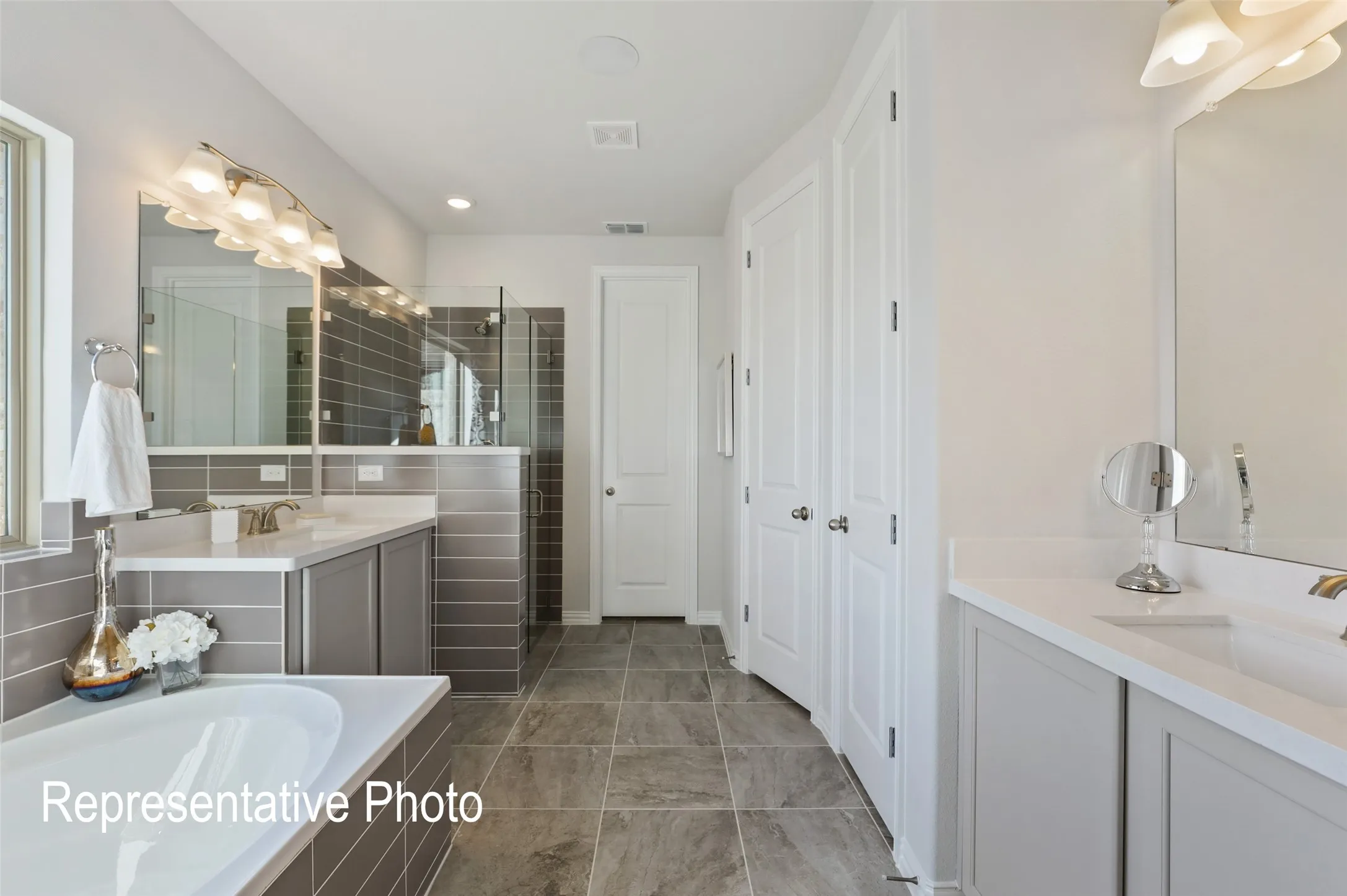 Spacious bathroom featuring a built-in tub, dual vanities with integrated sinks, a tiled shower enclosure with glass panels, and neutral-toned floor tiling