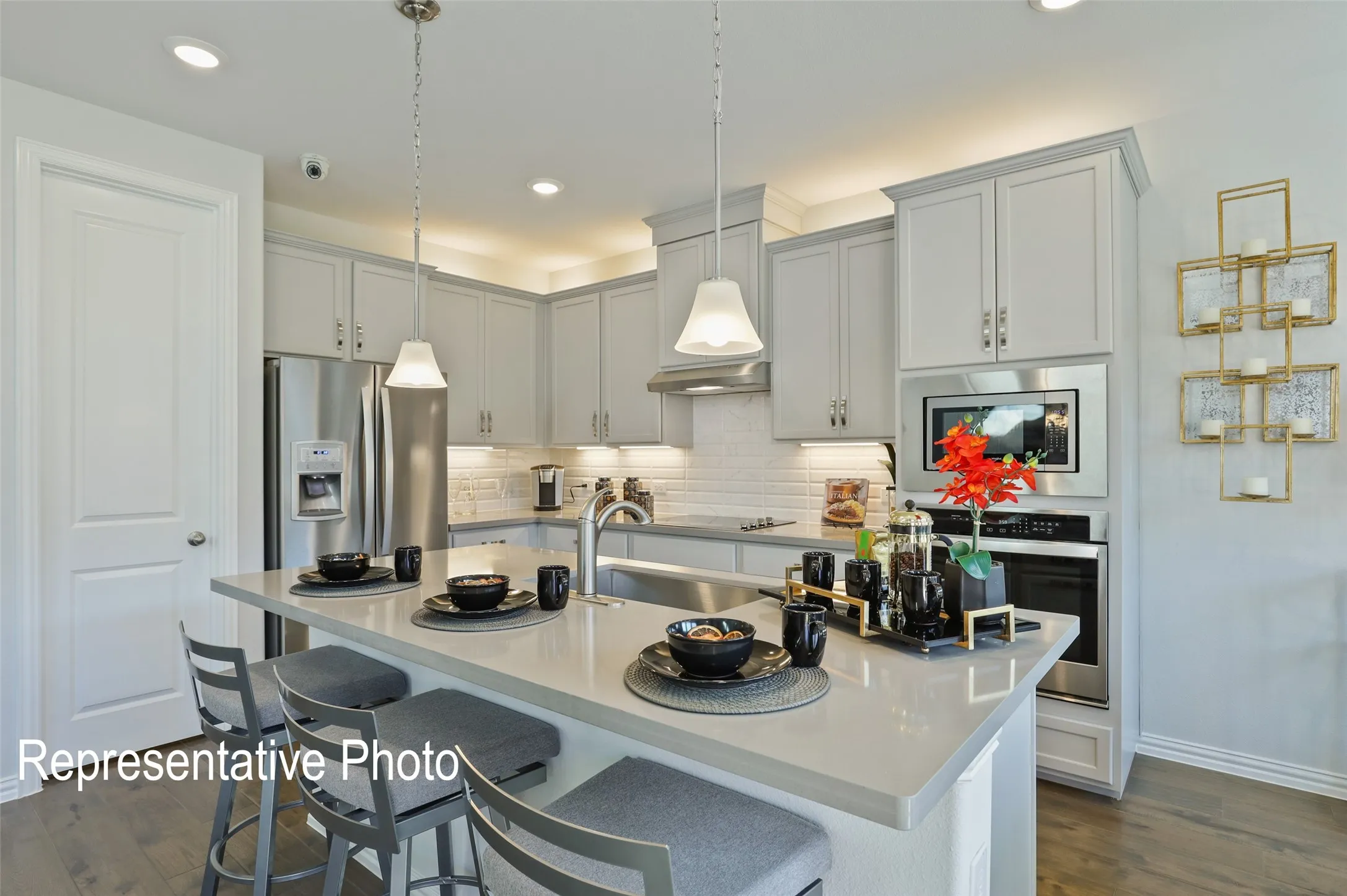 Modern kitchen featuring light gray cabinetry, stainless steel appliances, a center island with bar seating, pendant lighting, and wood-finish flooring