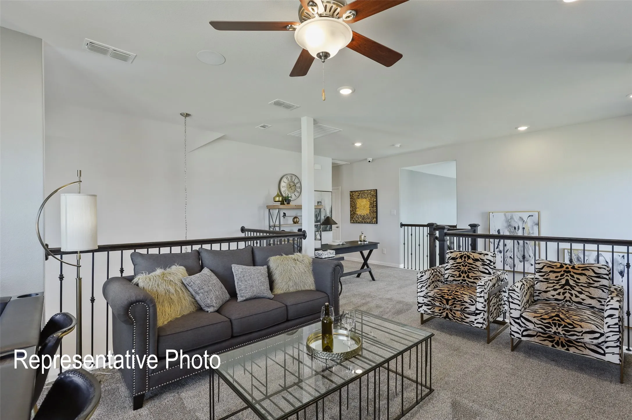 Spacious upper-level area featuring carpet flooring, recessed lighting, a ceiling fan with light fixture, and black metal railings overlooking the lower level
