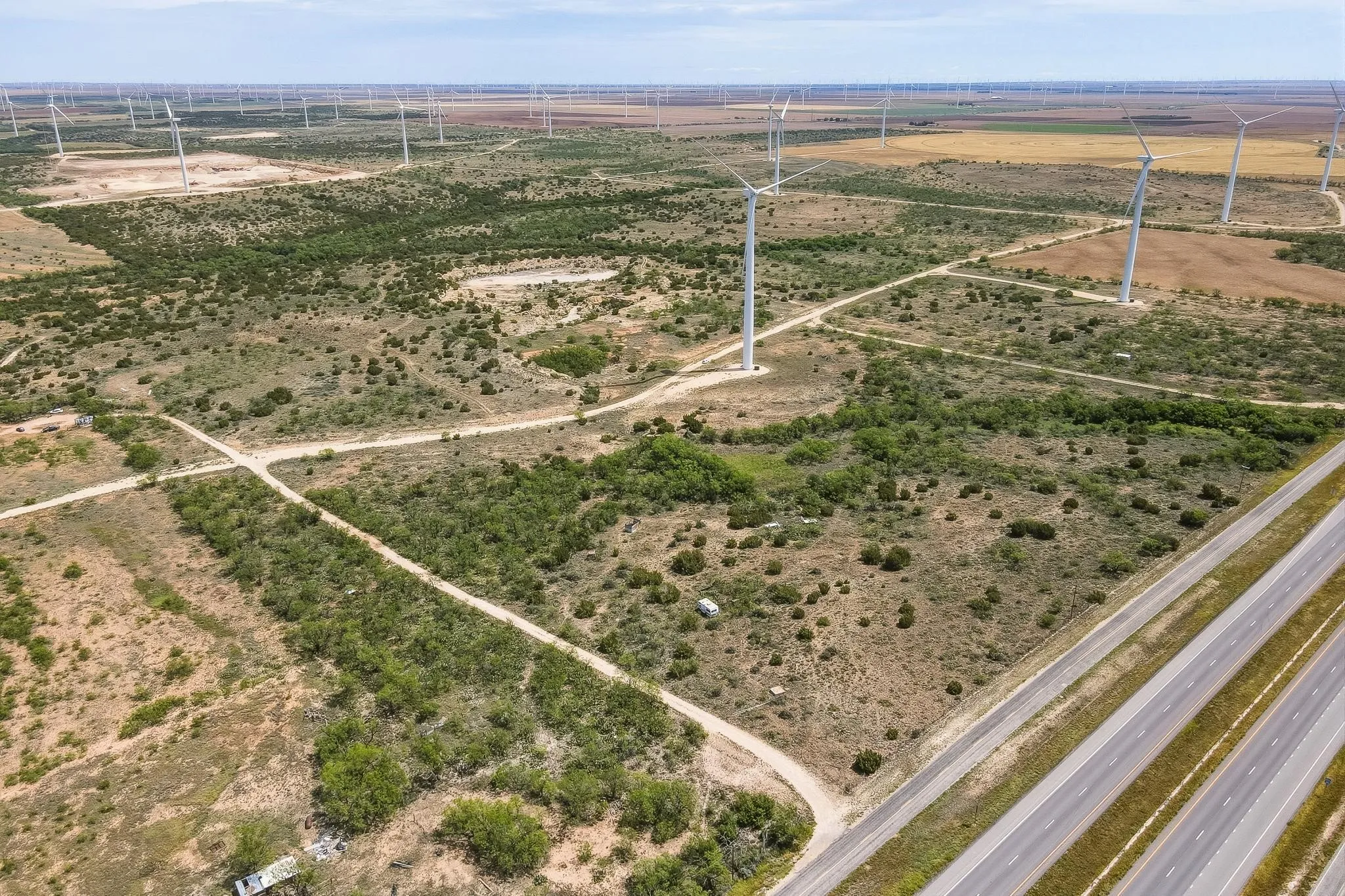 Expansive undeveloped land featuring natural vegetation, multiple wind turbines, and direct highway frontage