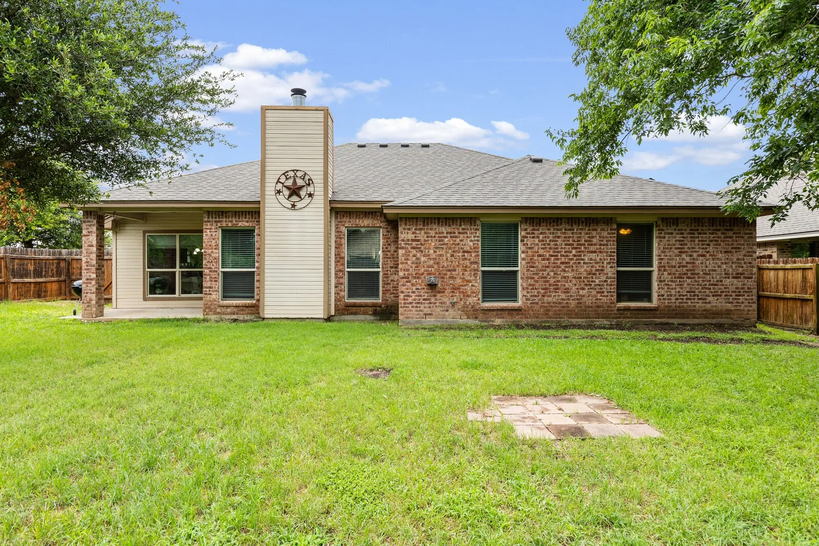 Expansive backyard featuring a brick exterior, covered patio, and a prominent chimney with decorative metalwork