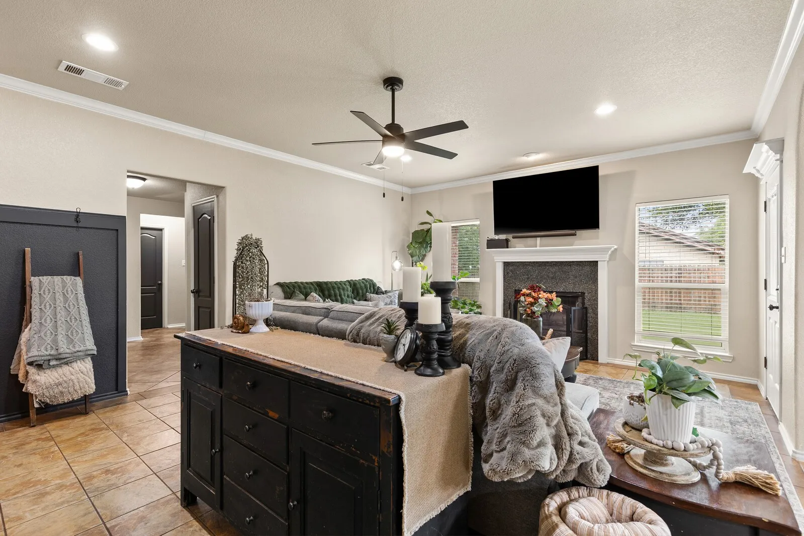 Open-concept living space with tile flooring, a fireplace featuring a dark stone surround and a white mantel, and crown molding