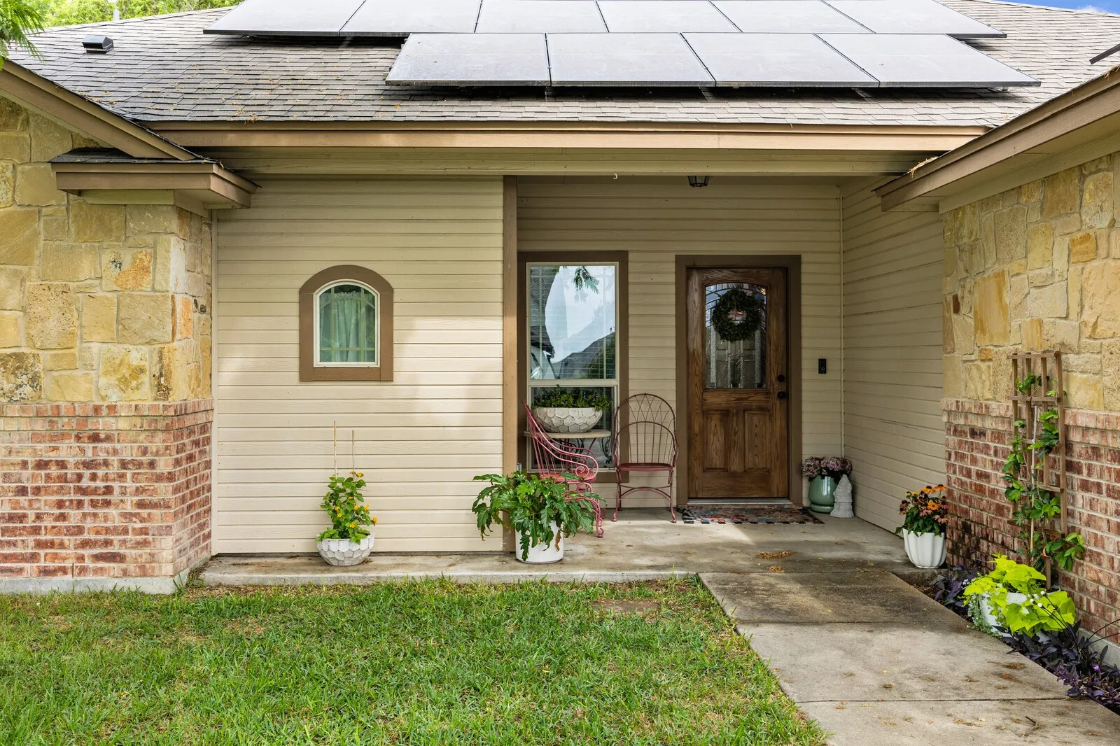 Front facade featuring a wood-panel entry door, complementary stone and brick accents, light-toned siding, and a gabled roofline with installed solar panels