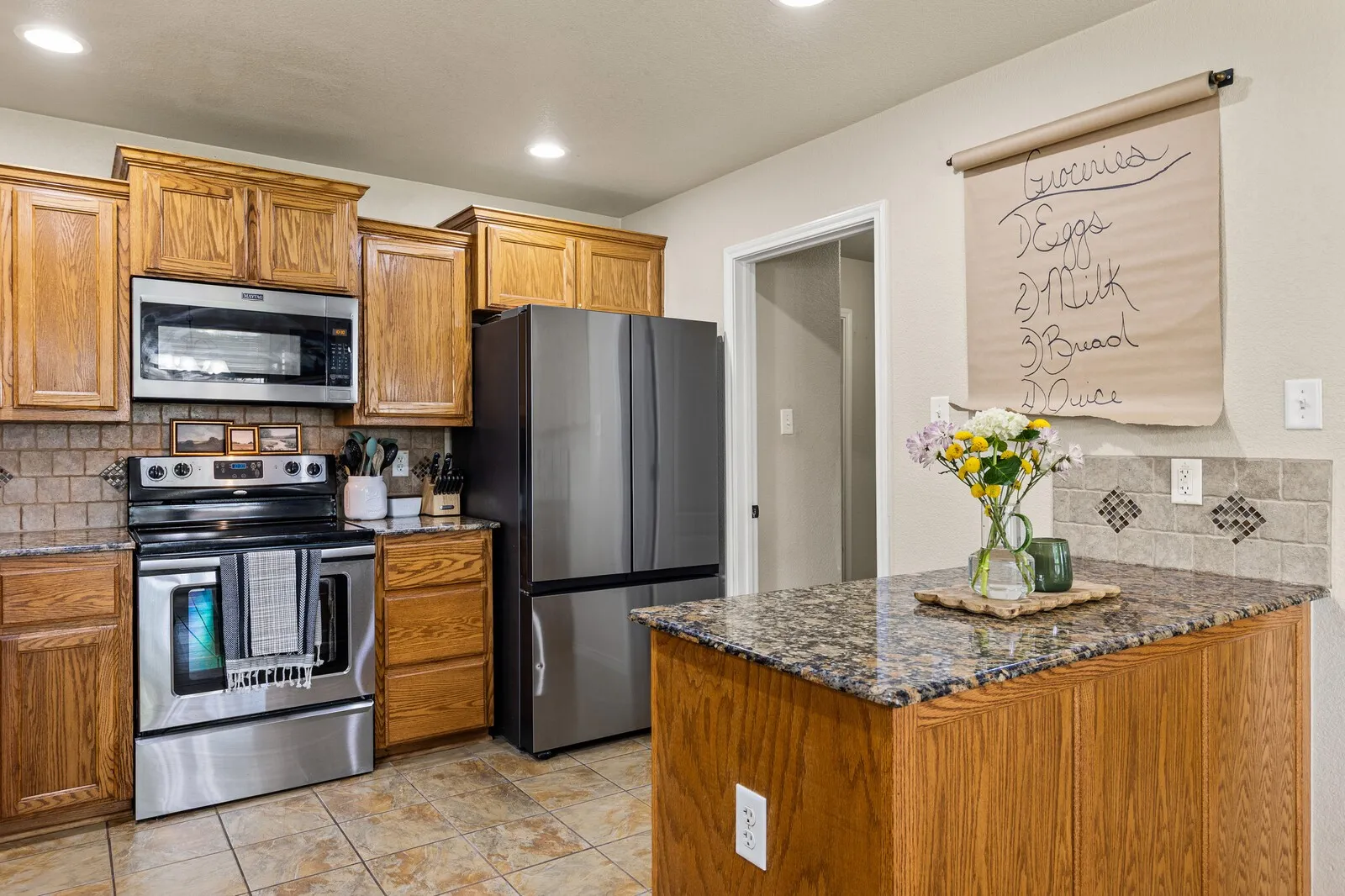 Kitchen featuring stainless steel appliances, wood cabinetry, stone countertops, and a tiled backsplash