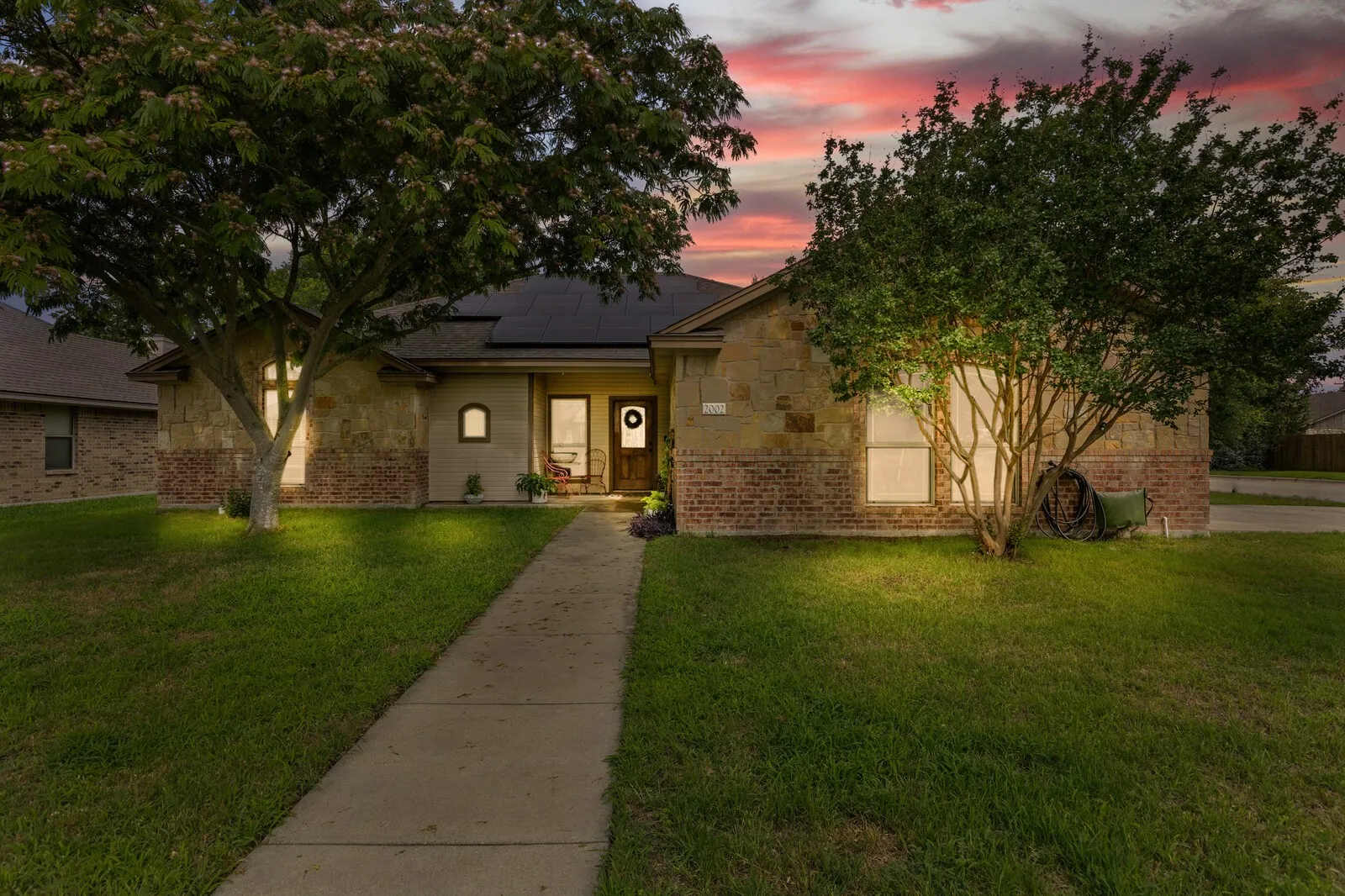 Stone and brick facade with mature trees and a concrete pathway leading to the front entry