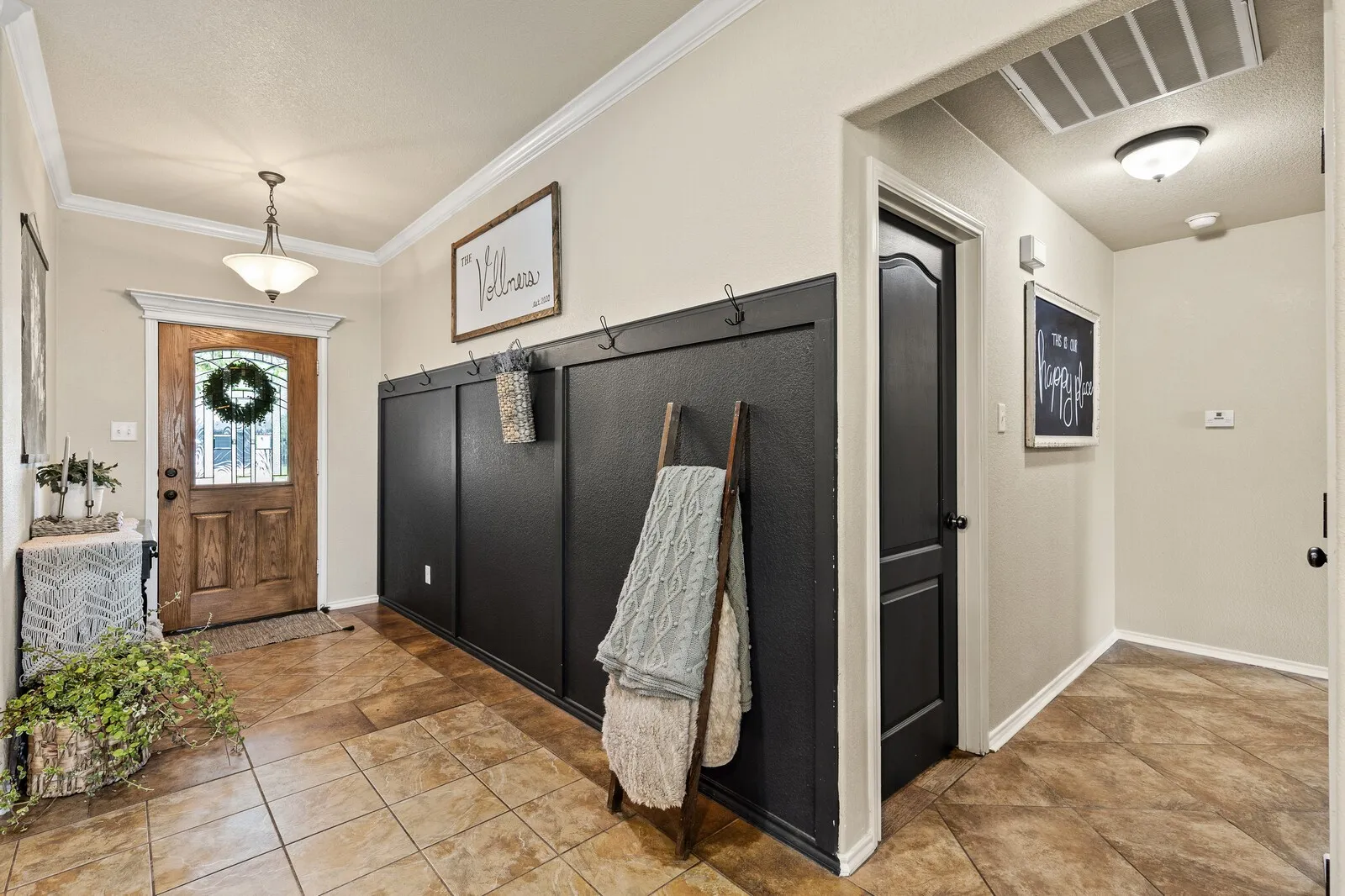 Entryway featuring warm-toned tile flooring, a paneled wood-finish front door with an integrated glass design, and a contrasting dark paneled accent wall with integrated hooks