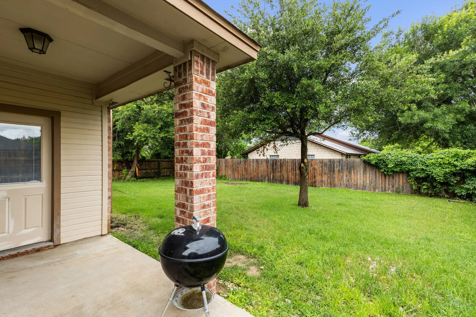 Covered patio with brick column, featuring a concrete surface and a side door with a window