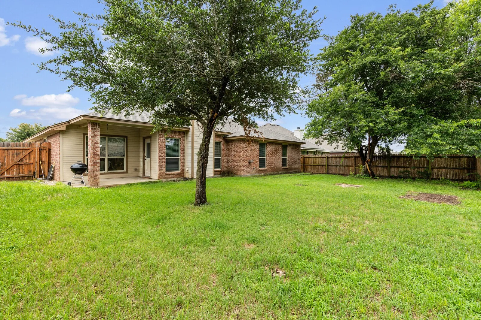 Expansive backyard featuring a manicured lawn, established trees, and a wooden privacy fence