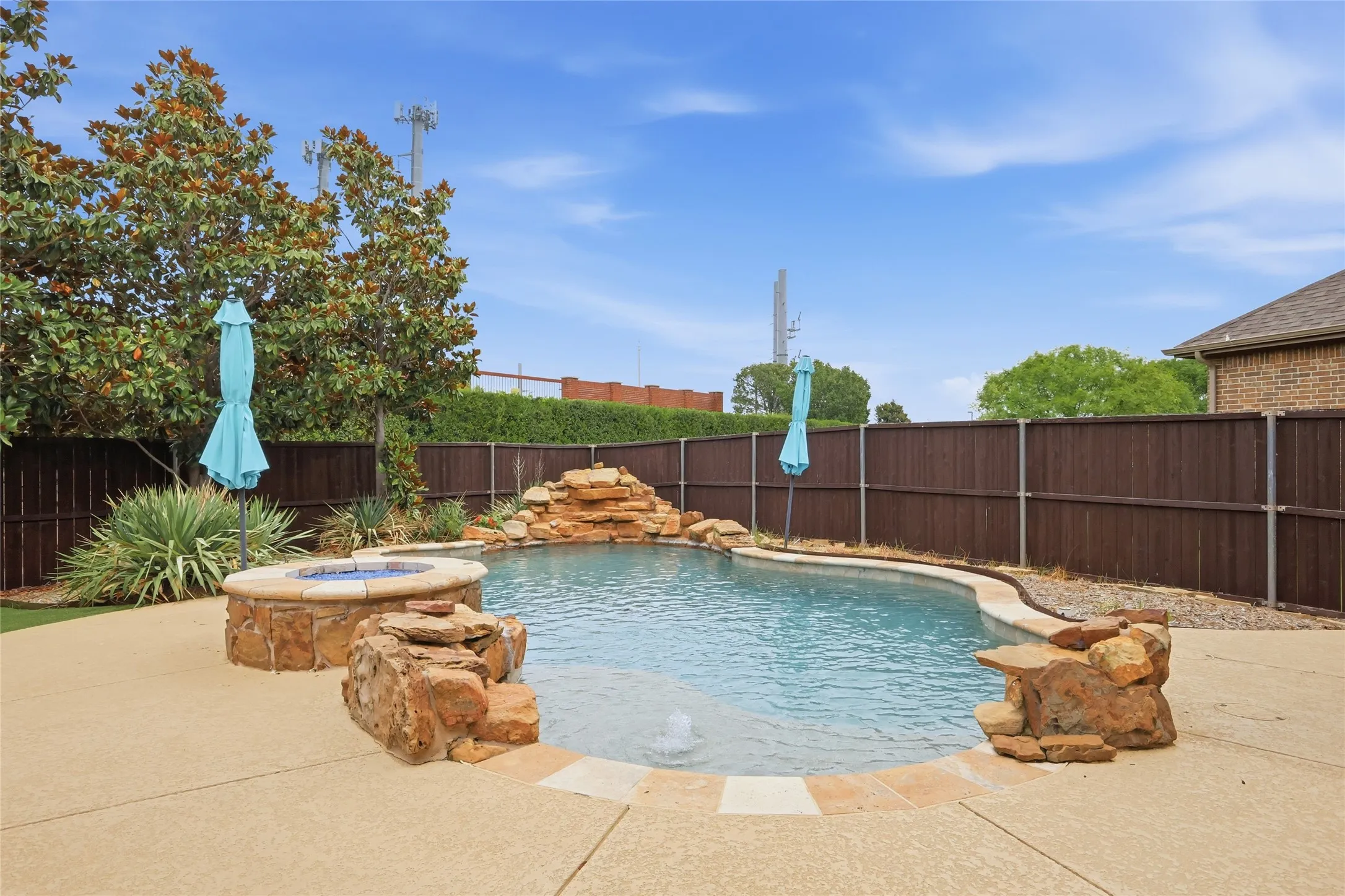 Custom-shaped swimming pool with a rock waterfall feature, integrated fire pit, and surrounding concrete decking