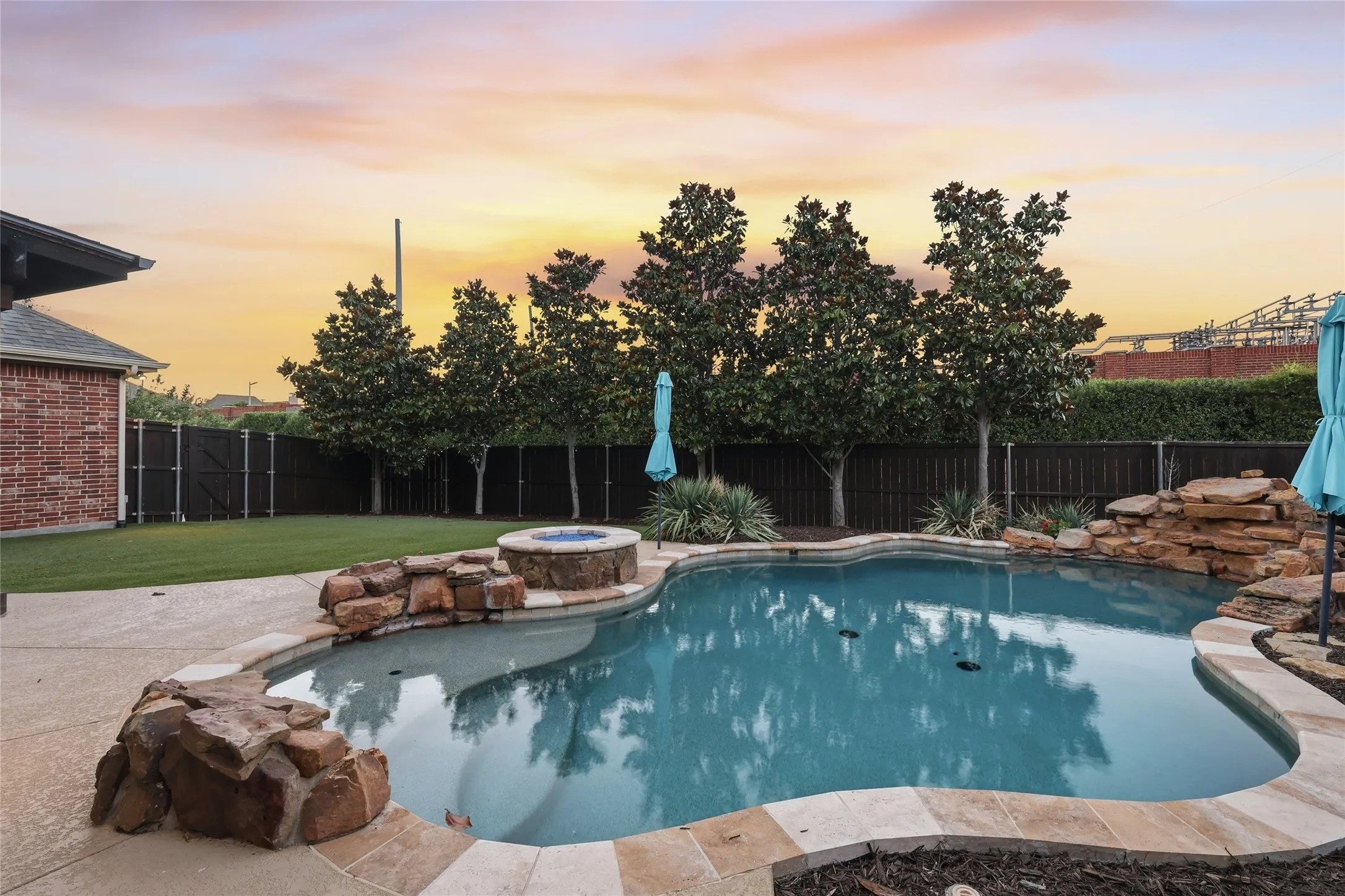 Freeform swimming pool with stone coping, an integrated fire pit, and a rock waterfall feature
