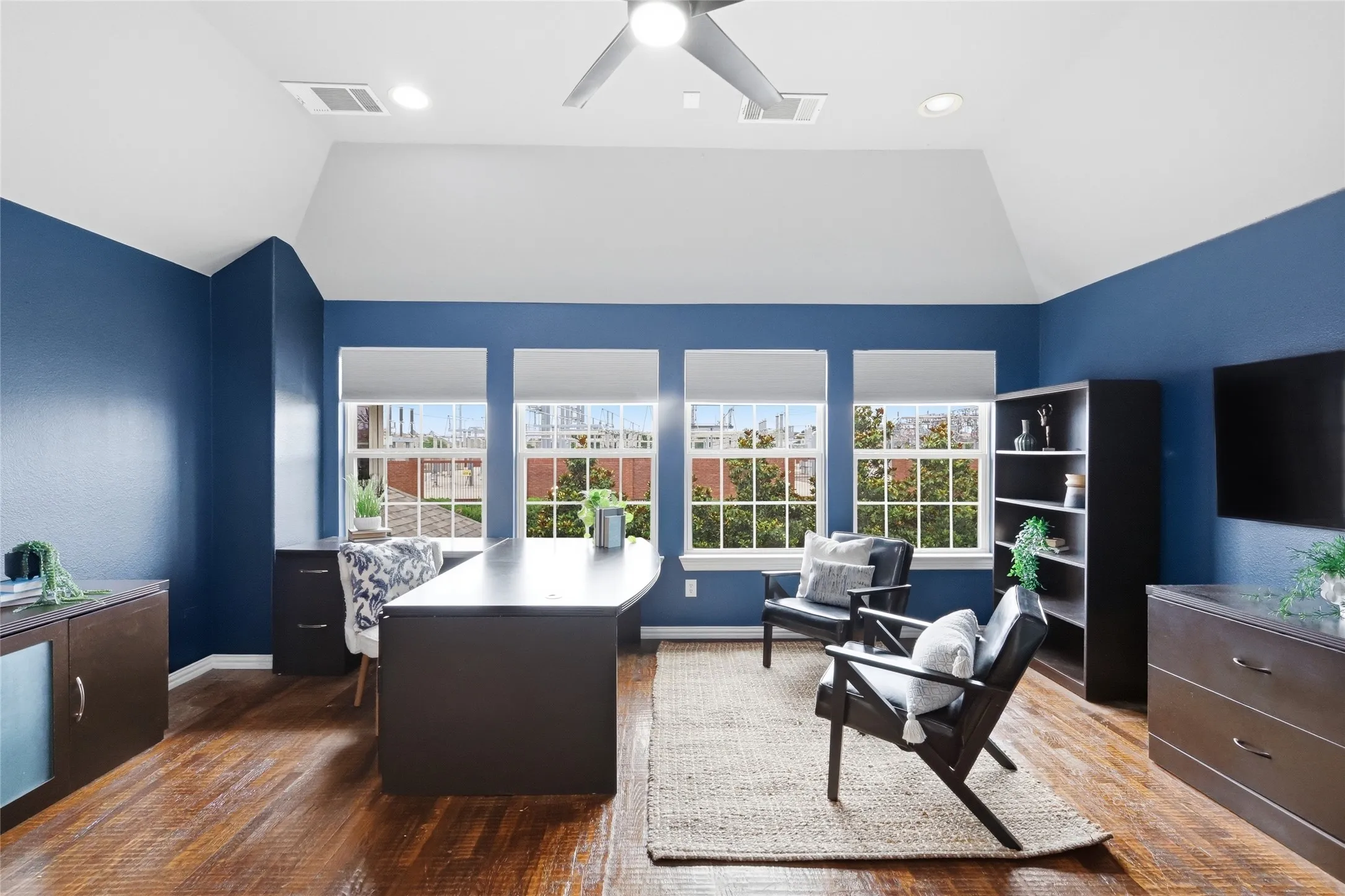 Vaulted ceiling with recessed lighting and ceiling fan, wood-finish flooring, and multiple windows with roller shades