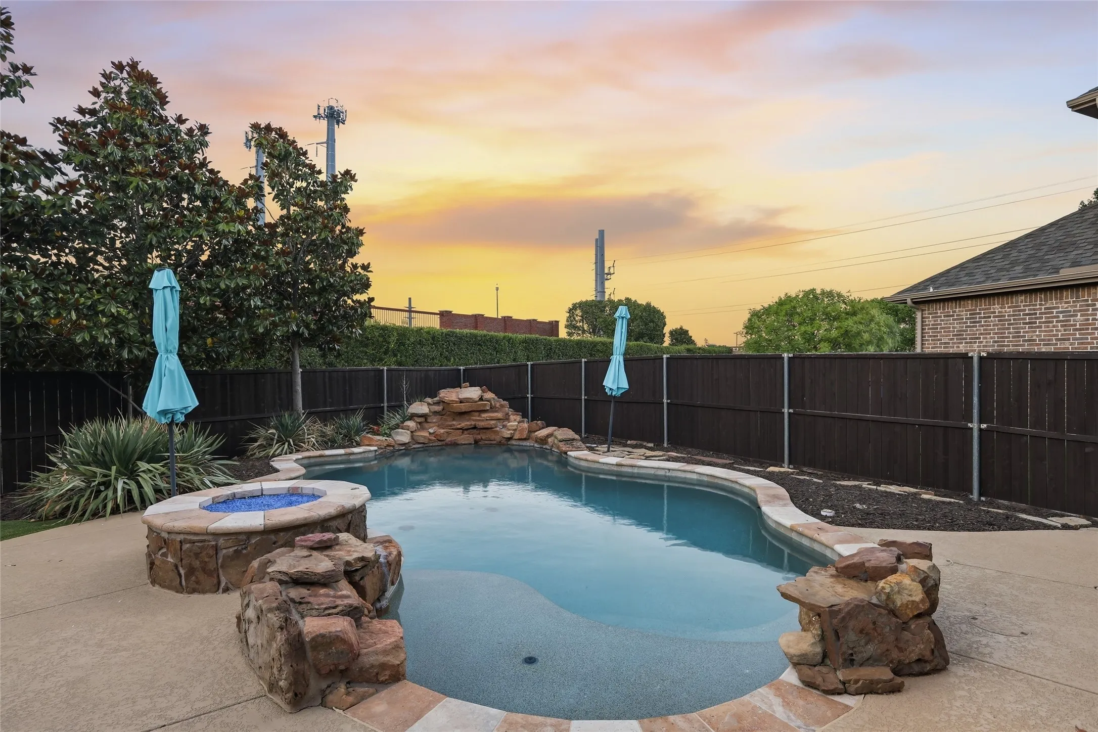 Freeform swimming pool with a rock waterfall feature, integrated fire pit, and concrete decking