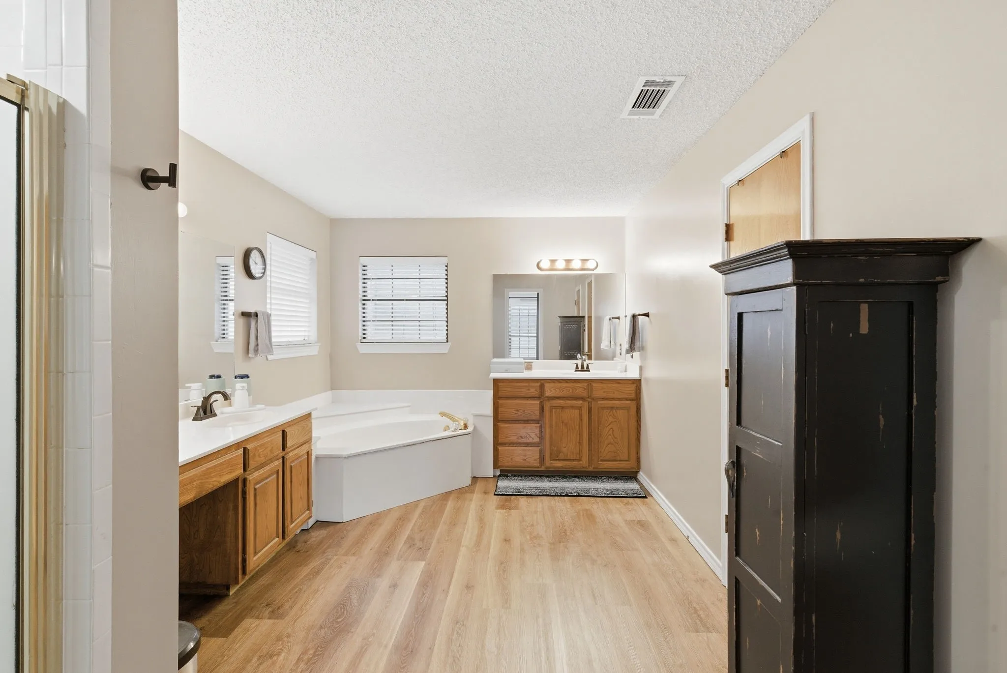 Bathroom featuring wood-finish flooring, a corner soaking tub, dual vanity with wood cabinetry, and a shower enclosure