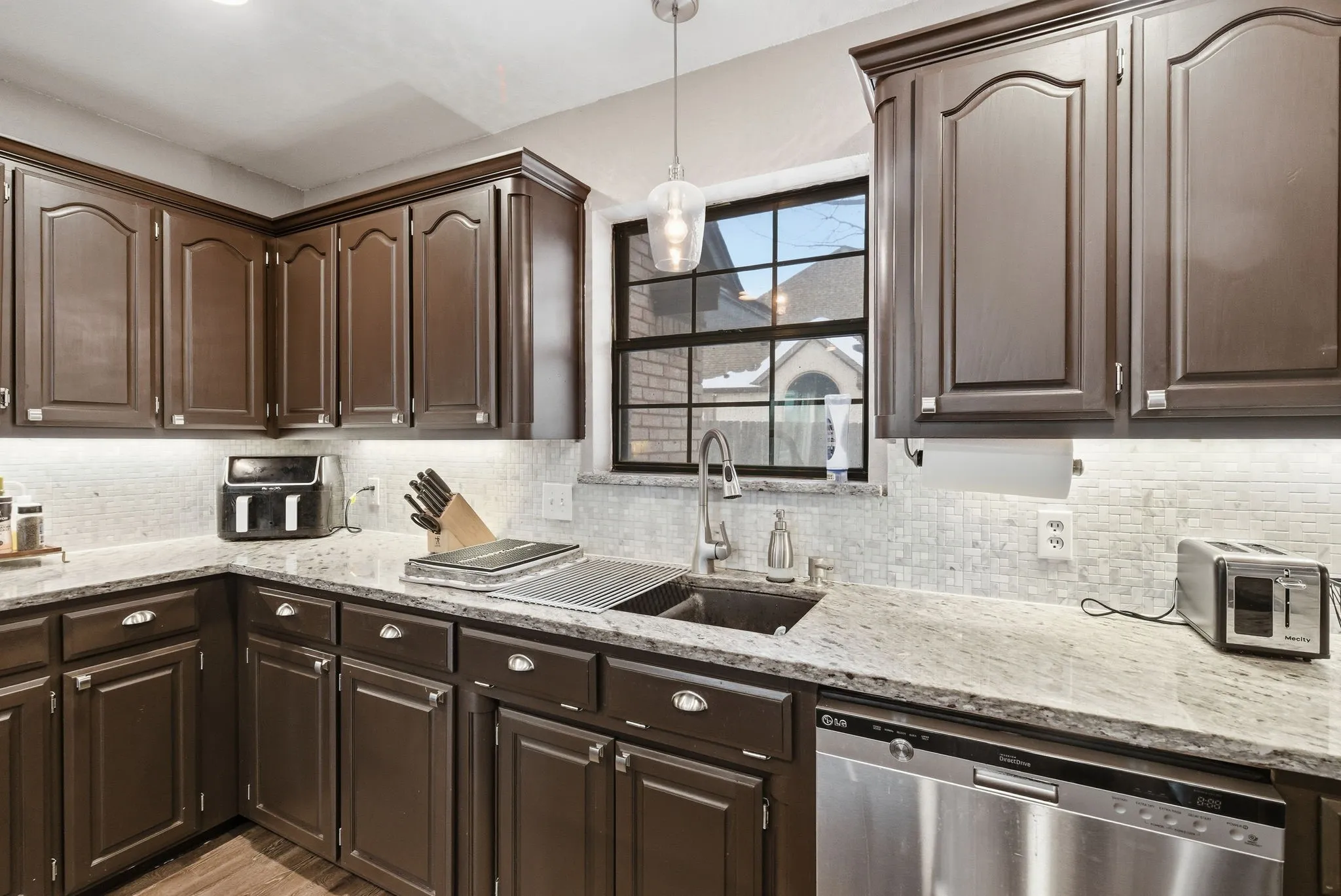 Kitchen featuring granite countertops, dark wood cabinetry, a mosaic tile backsplash, stainless steel appliances, and a window above the sink