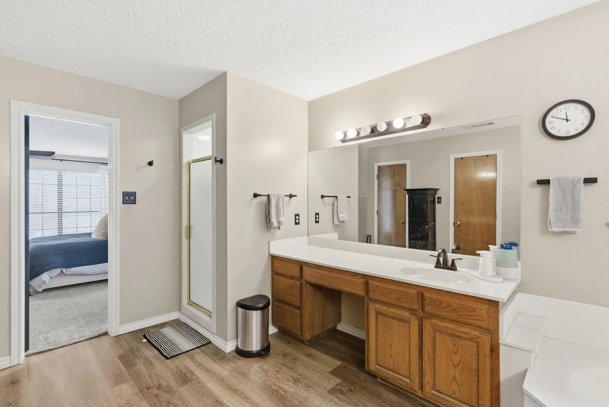 Bathroom featuring wood-finish flooring, a double vanity with white countertops, and a full-width mirror