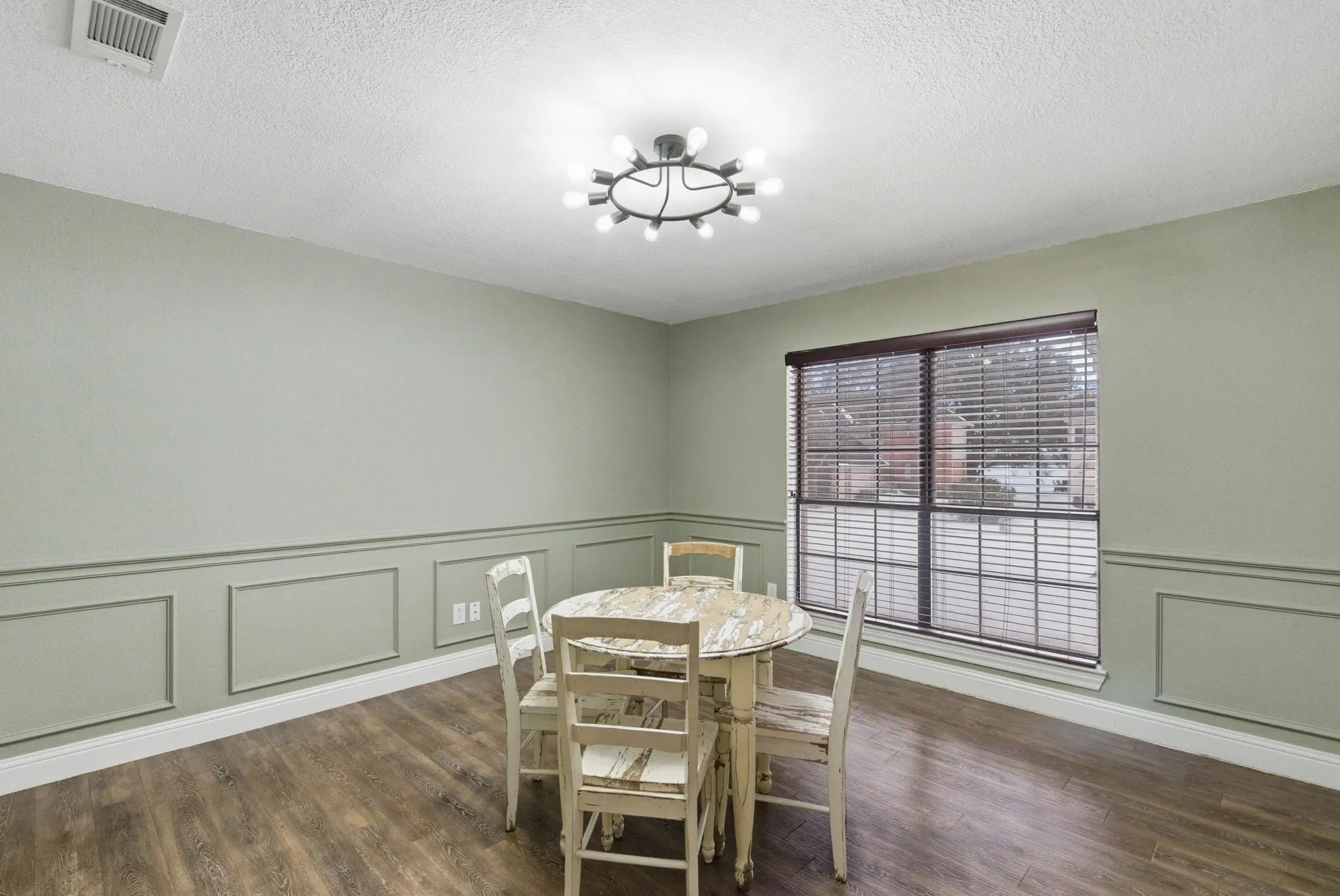 Dining area featuring wood-finish flooring, wainscoting paneling, and a contemporary ceiling light fixture