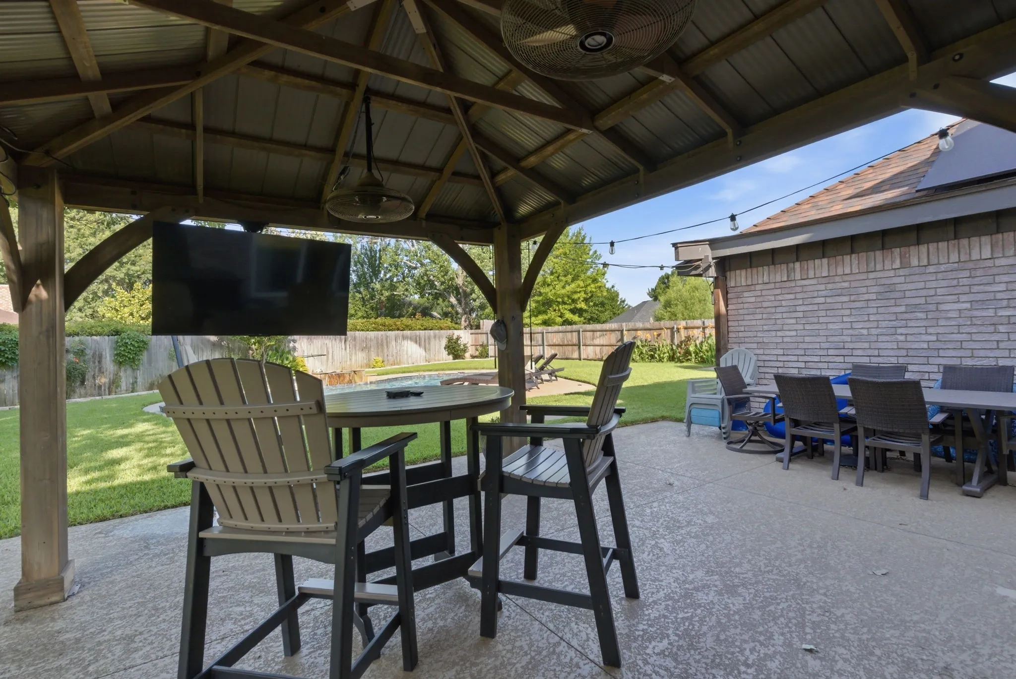Spacious outdoor patio area featuring a covered gazebo with built-in ceiling fans, a flat-screen television mount, and string lighting