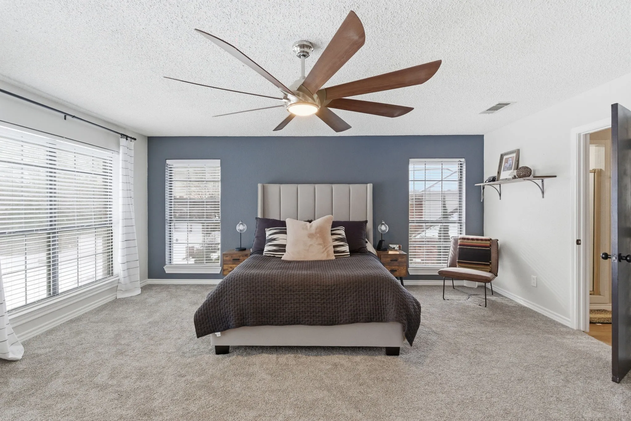 Spacious room featuring light gray carpeting, a decorative ceiling fan with wood-finish blades, and a prominent accent wall in a deep blue tone