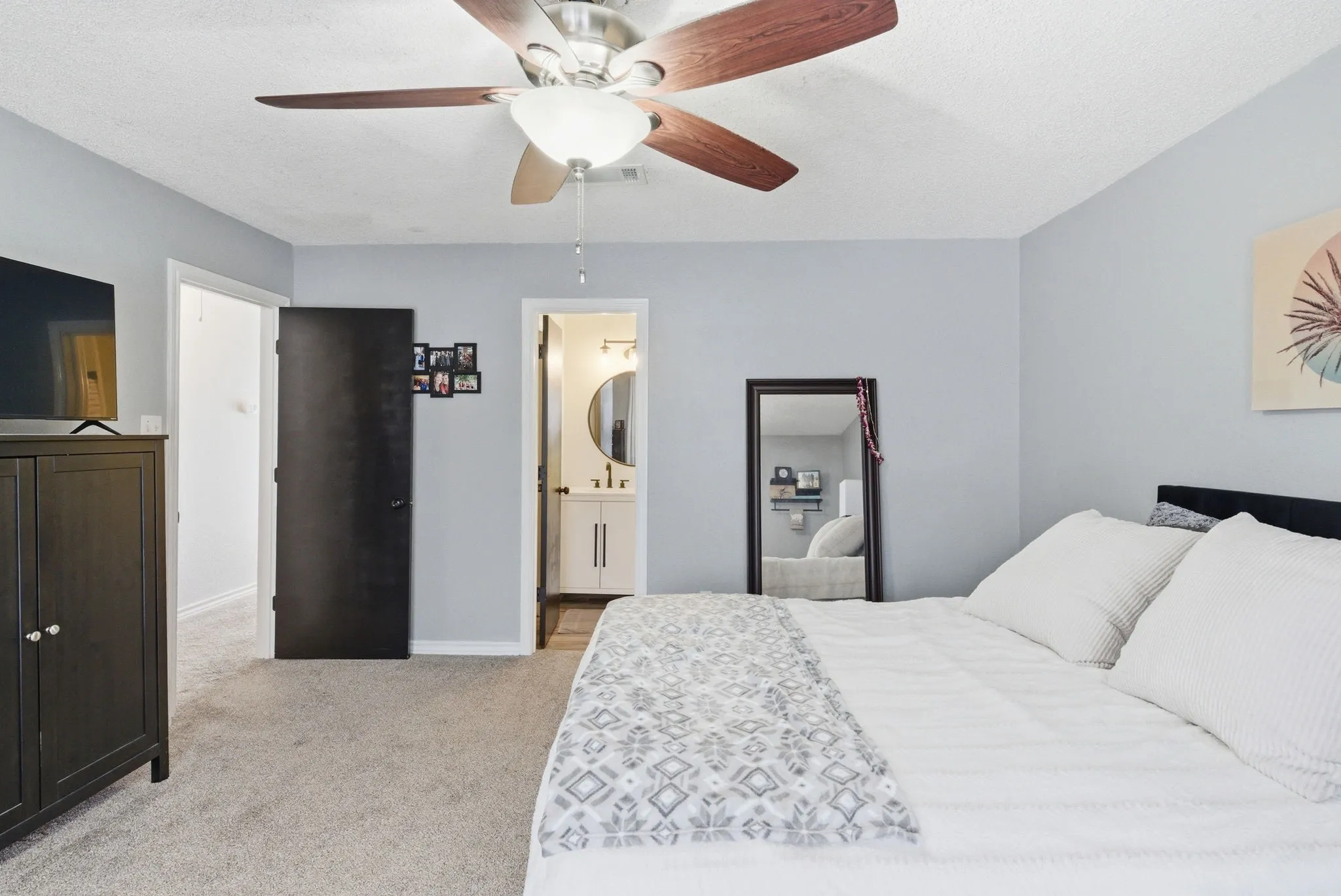 Carpeted room featuring a ceiling fan with wood-finish blades, light gray wall paint, and a dark-paneled door