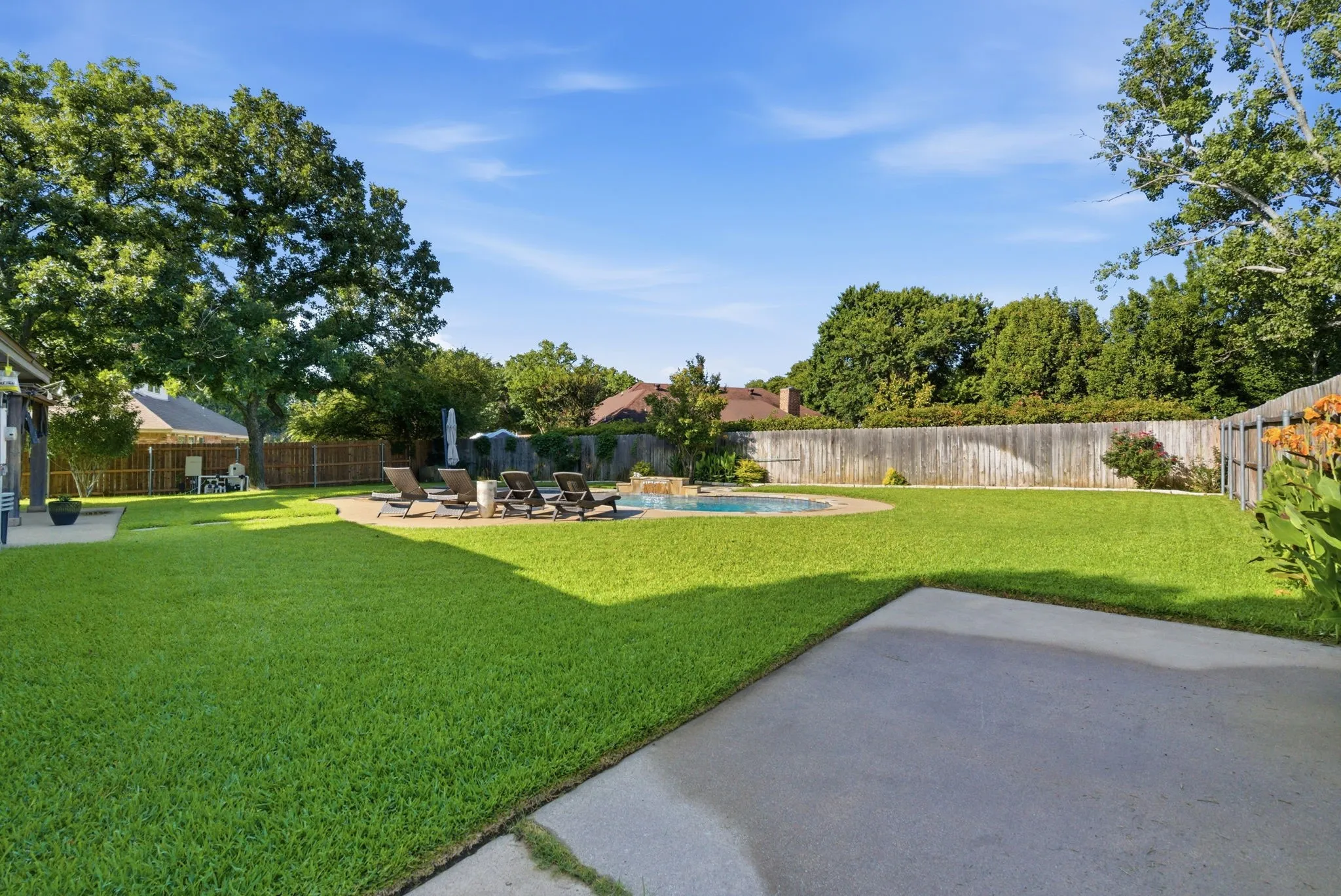 Spacious backyard featuring a rectangular concrete patio, expansive lawn area, and a built-in swimming pool with surrounding hardscaping