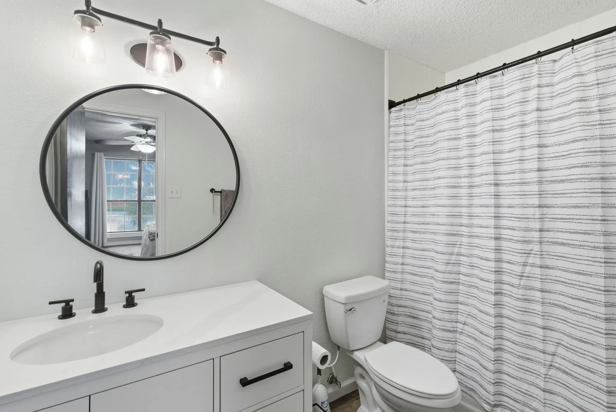 Bathroom vanity with a white countertop and integrated sink, complemented by a round framed mirror and matte black fixtures