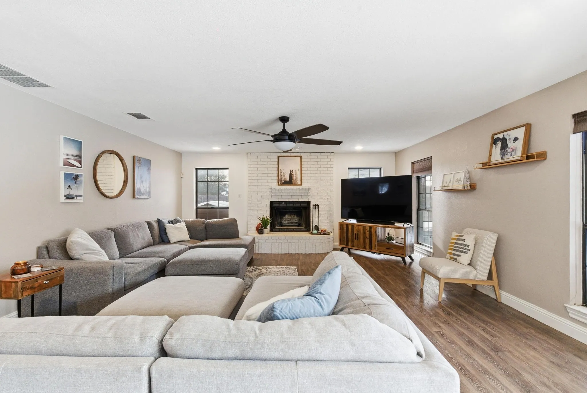 Spacious living area featuring wood-finish flooring, a white-painted brick fireplace, and a ceiling fan