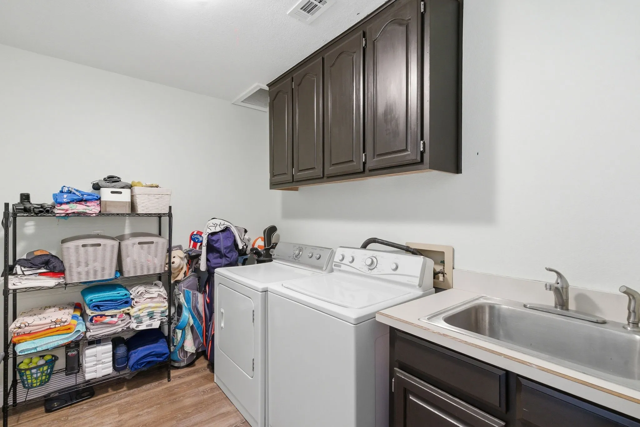 Dedicated laundry area featuring wood-finish flooring, dark cabinetry, and a utility sink