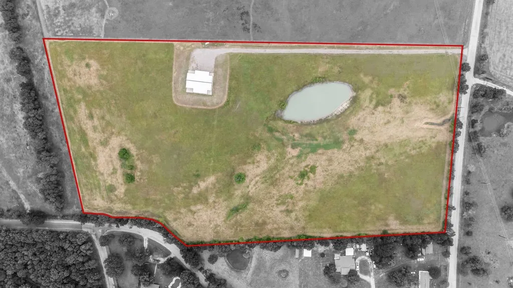 Expansive parcel featuring a large pond, perimeter fencing, and a building structure