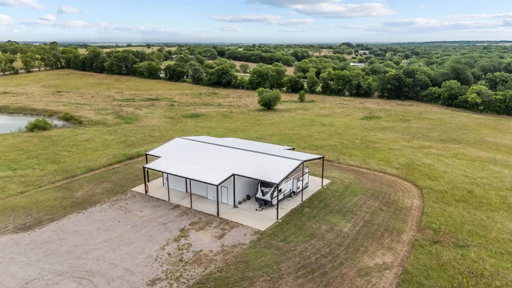 Expansive pole barn with a white metal roof and concrete slab, featuring ample covered parking and a gravel driveway